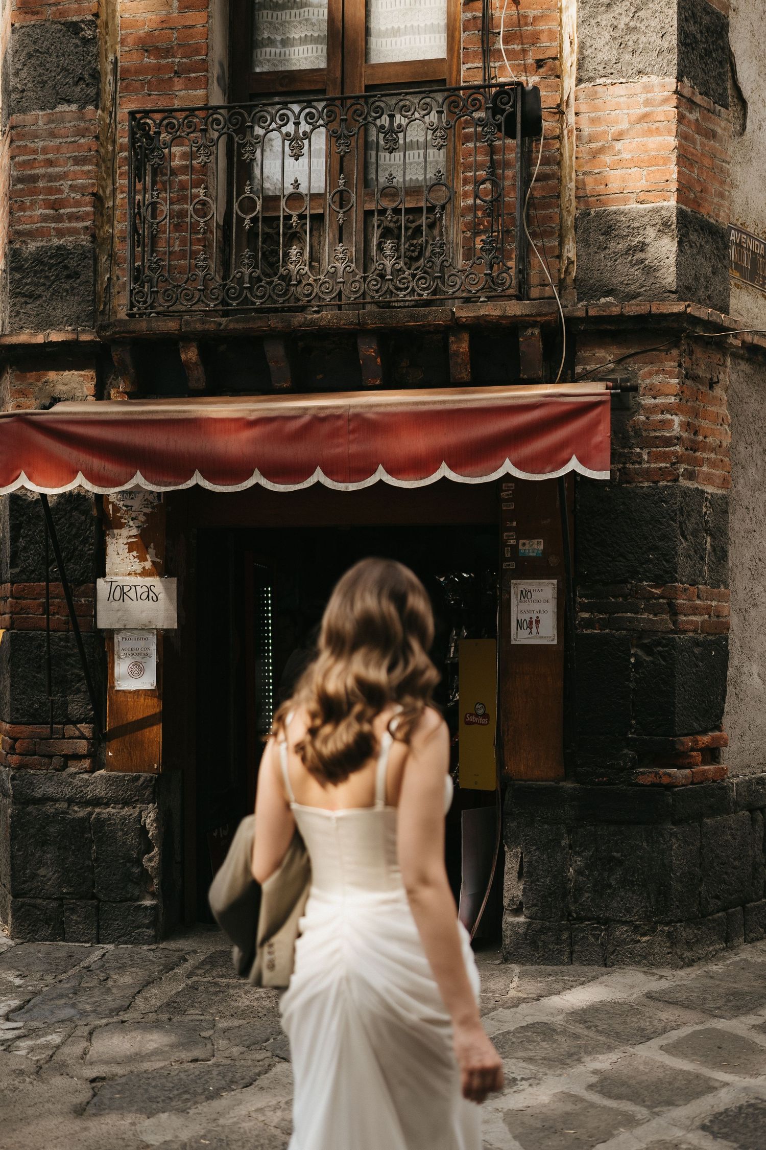 A person in a white dress walks through a rustic brick archway entrance.