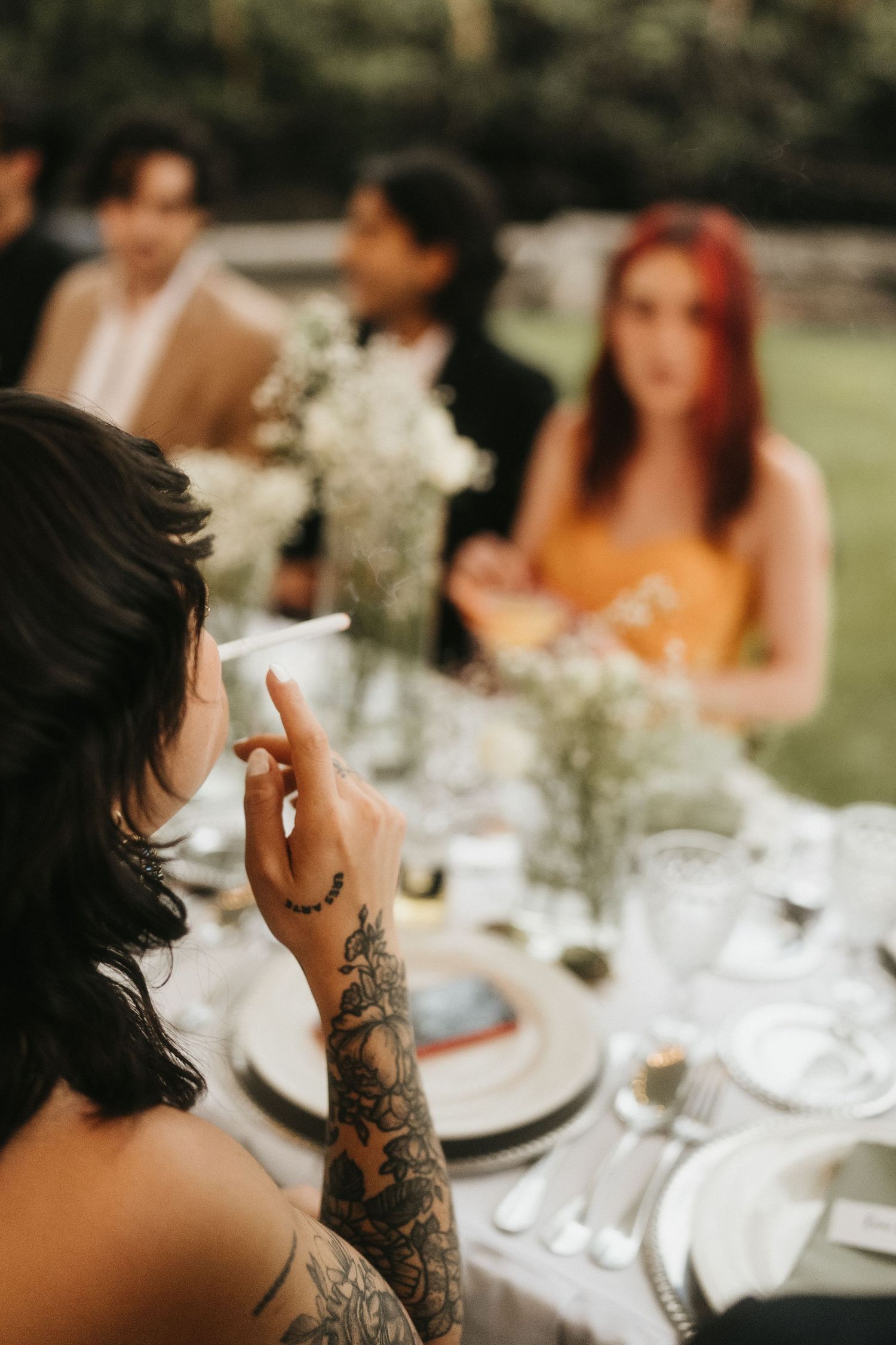 Wedding reception table detail showing tattooed arm reaching for a glass among place settings.