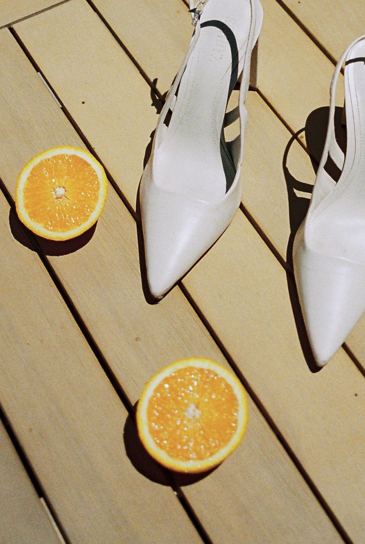 White bridal shoes and sliced oranges arranged on wooden deck planks.