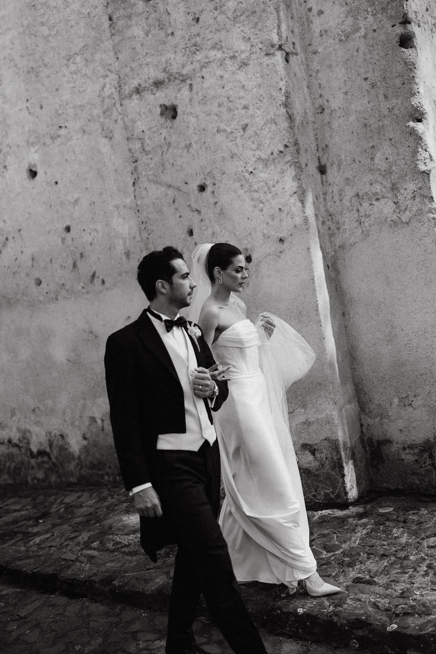 Black and white photo of a couple in formal attire against a textured wall.