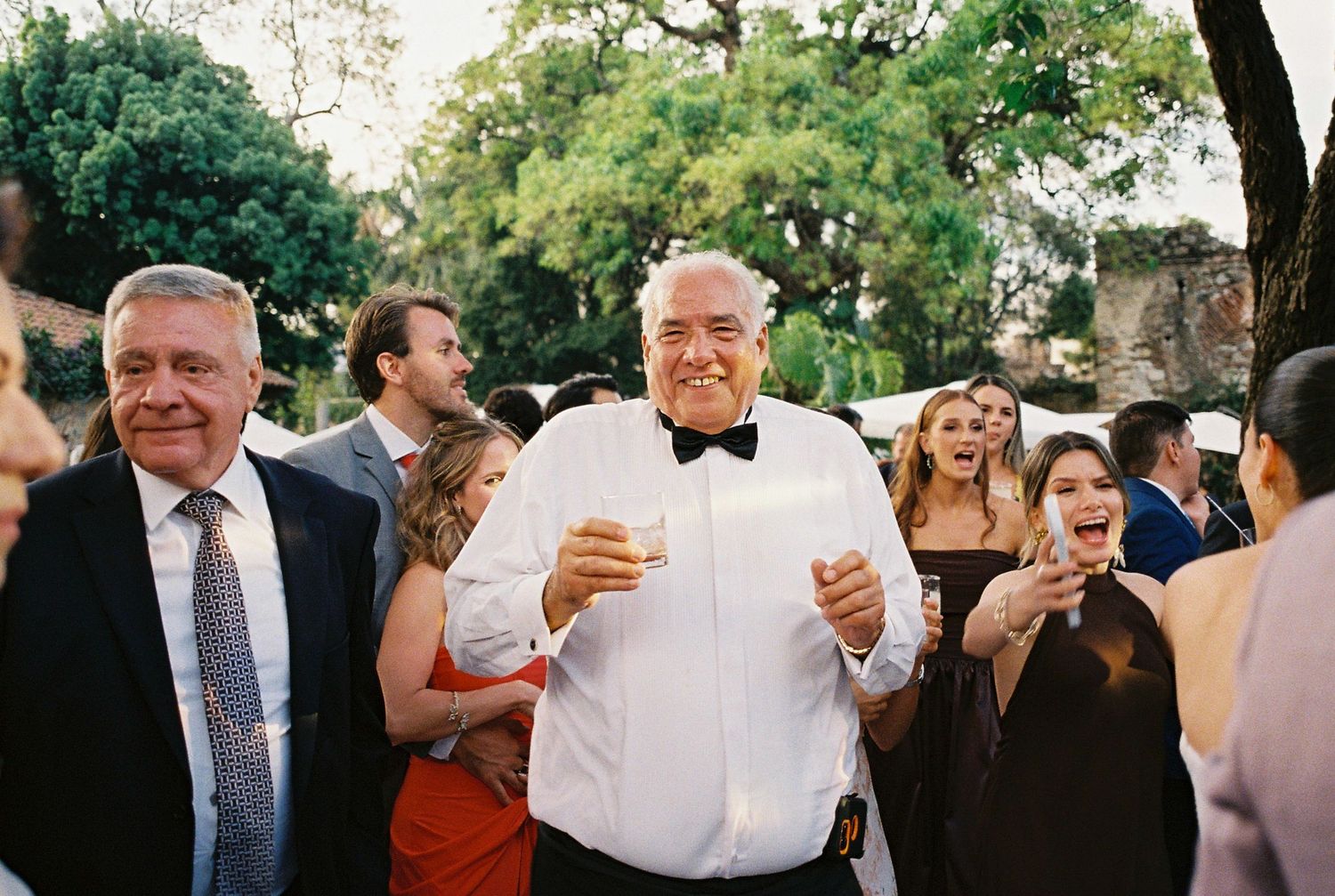 Wedding guests raise their glasses in a joyful outdoor toast during a celebration.