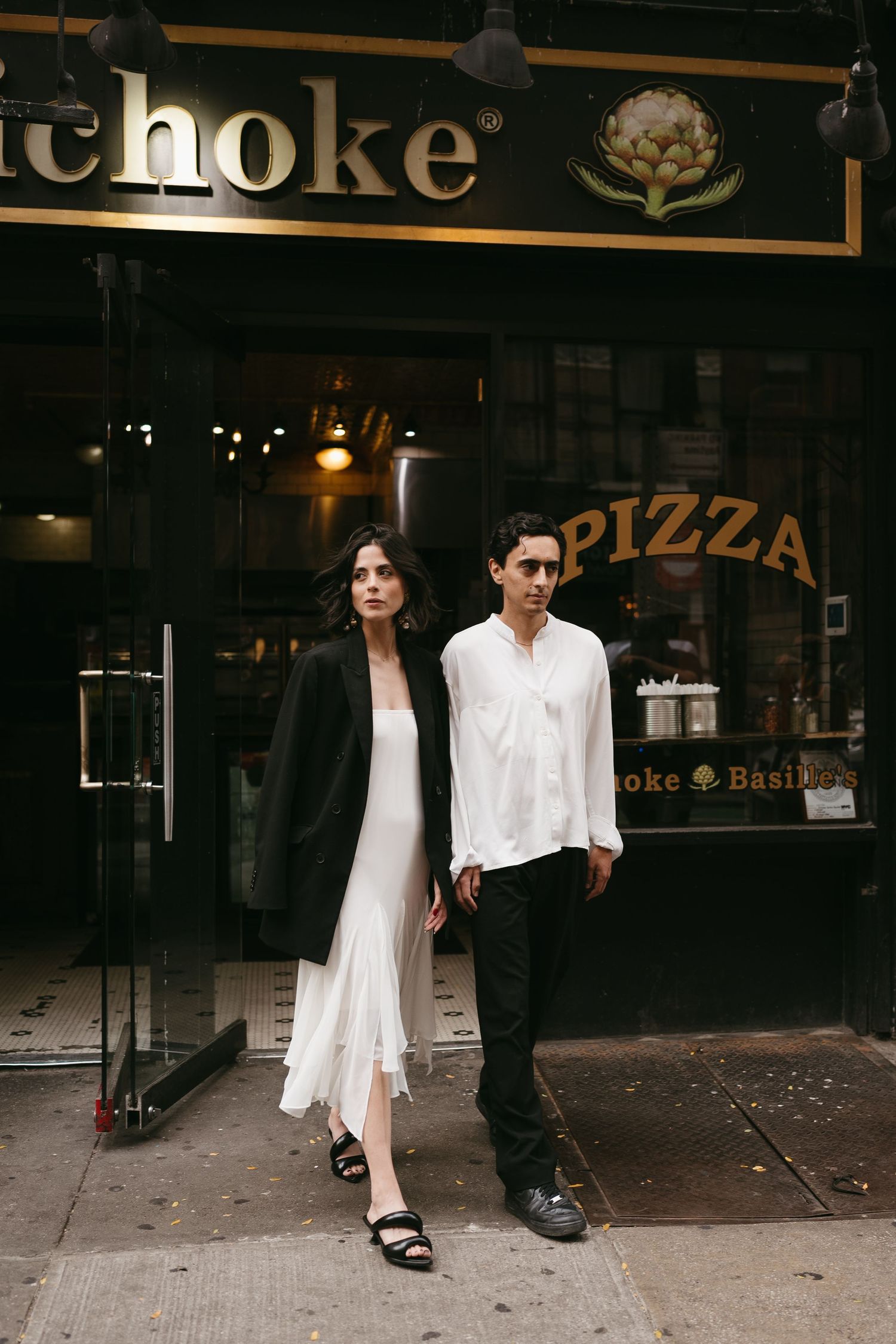 Urban street scene outside pizza shop with couple in contrasting black and white outfits.