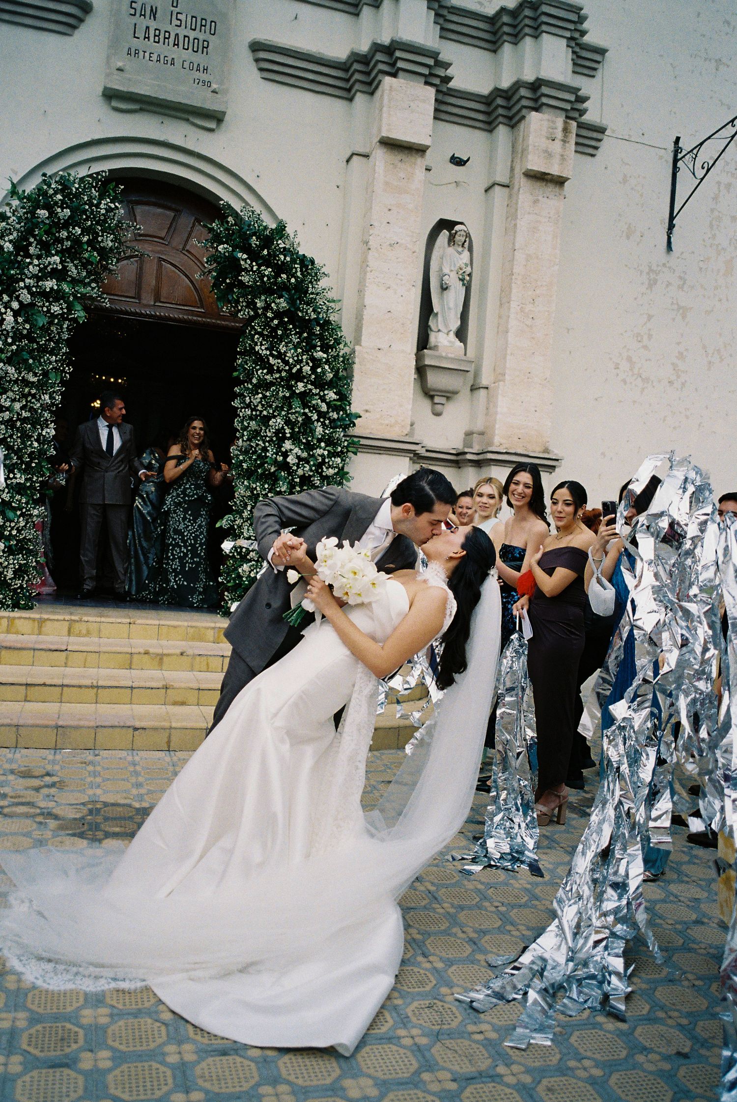 Wedding celebration outside historic church with flowing white dress and dancing guests.