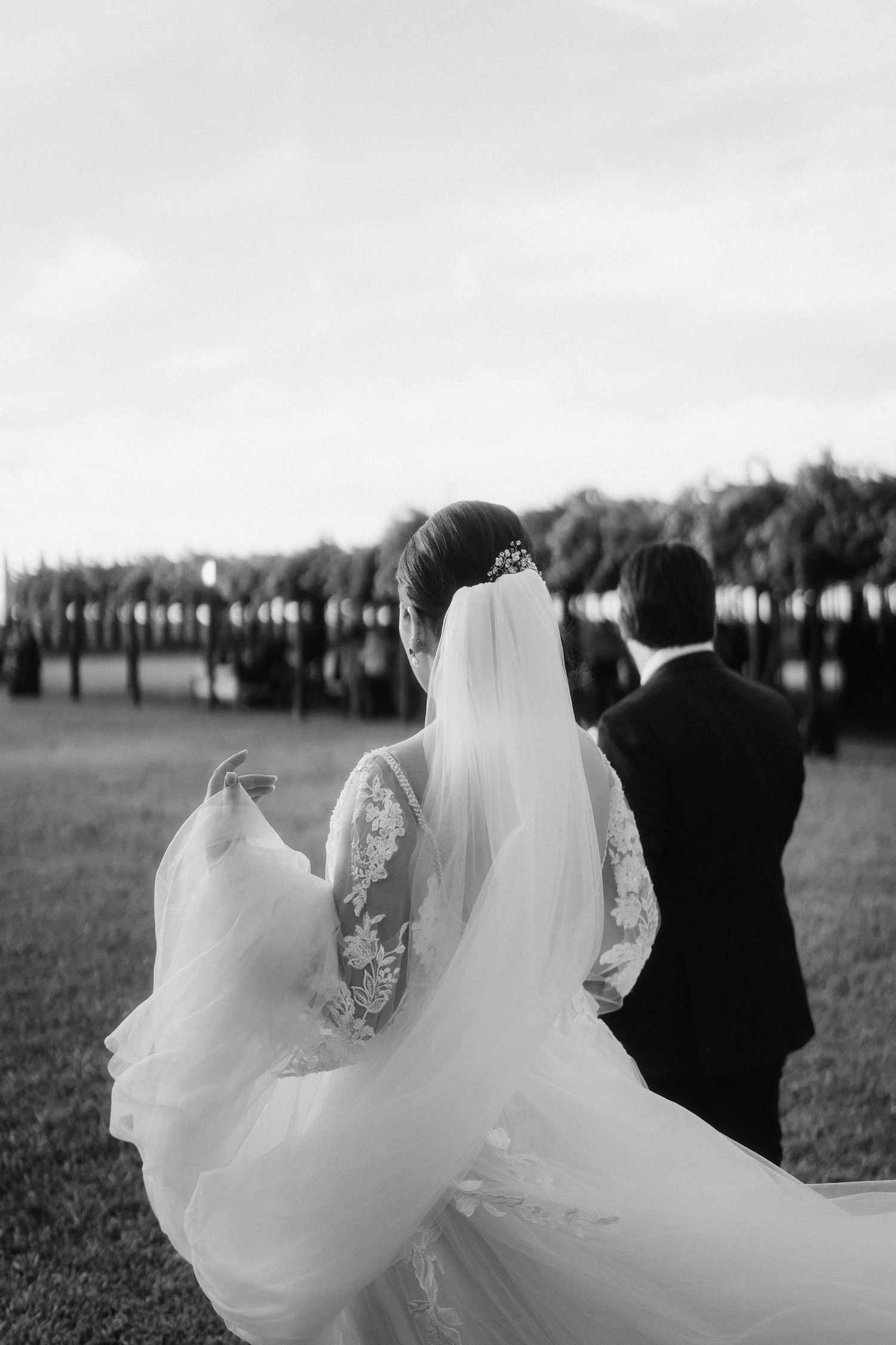 Black and white photo of a flowing wedding dress train in motion outdoors.