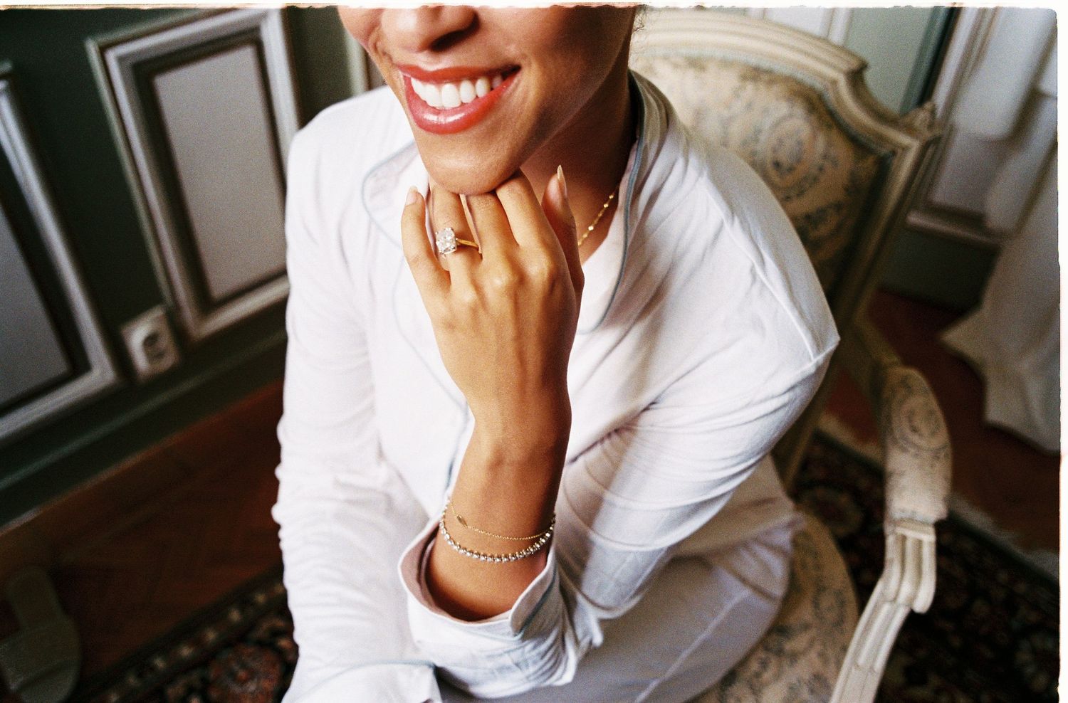 A person in a white button-down shirt smiles while sitting indoors.