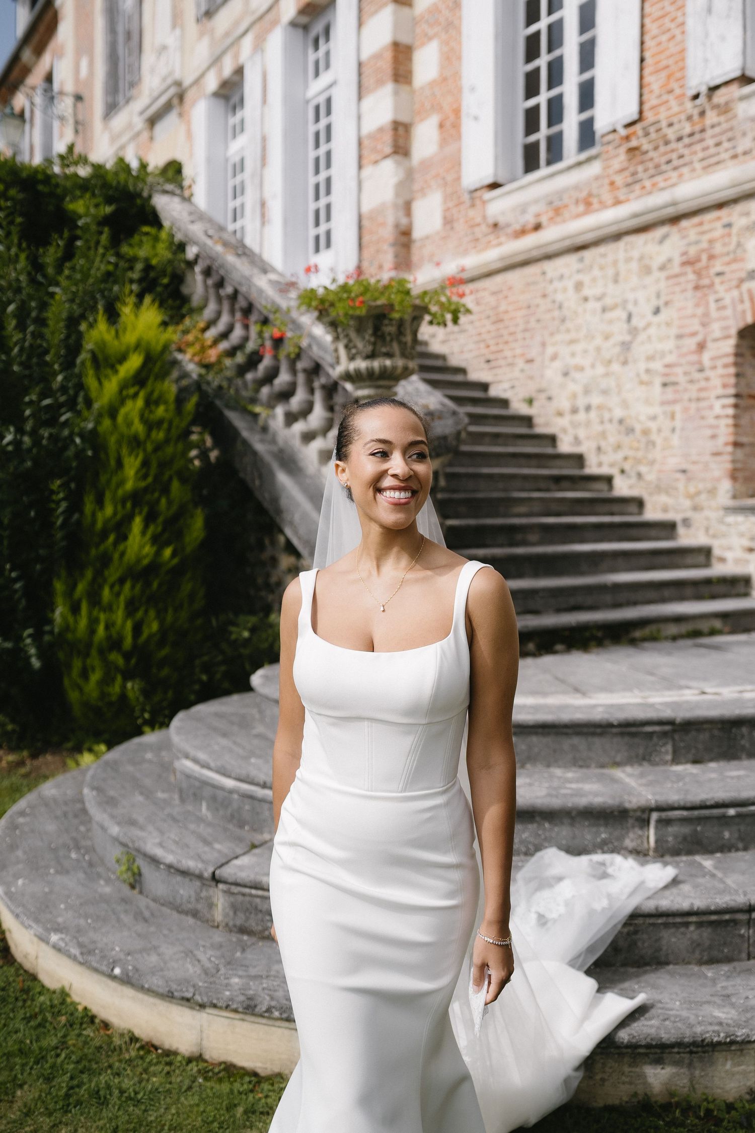 A bride in a white dress poses on historic stone steps near a brick building.