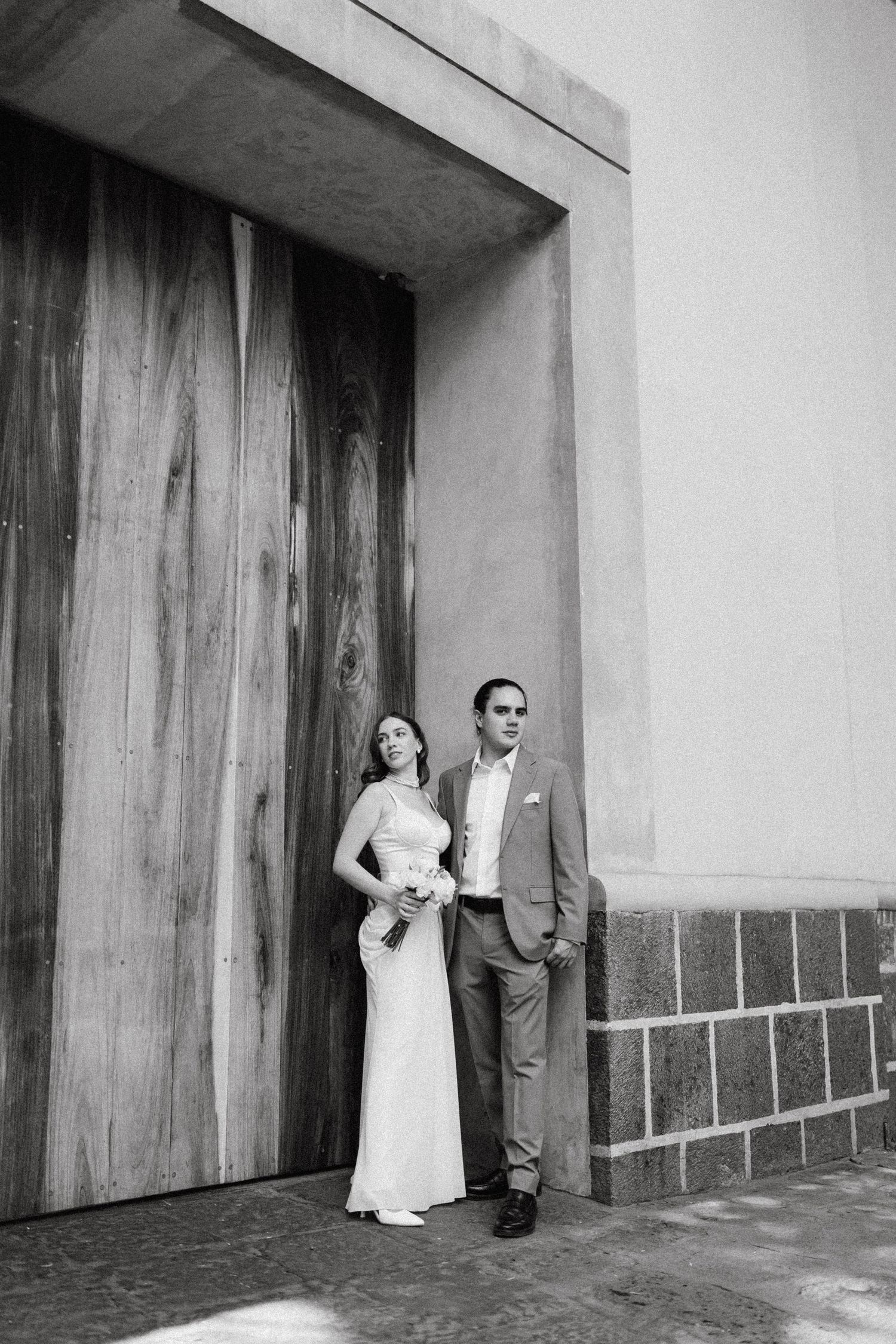 A series of black and white wedding photos against wooden doors and concrete walls.