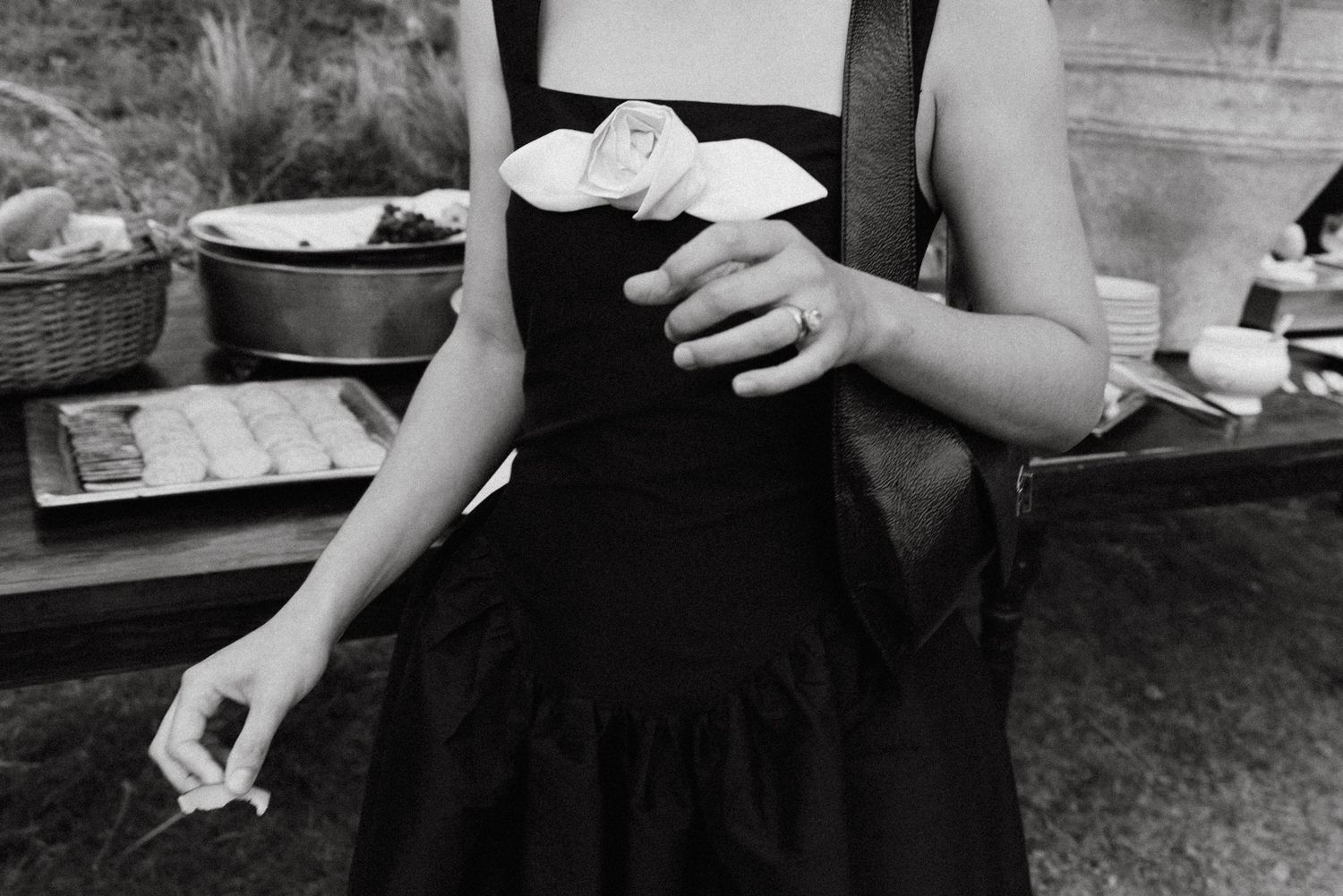 A black and white photo showing hands holding a drink in a black dress at an outdoor gathering.