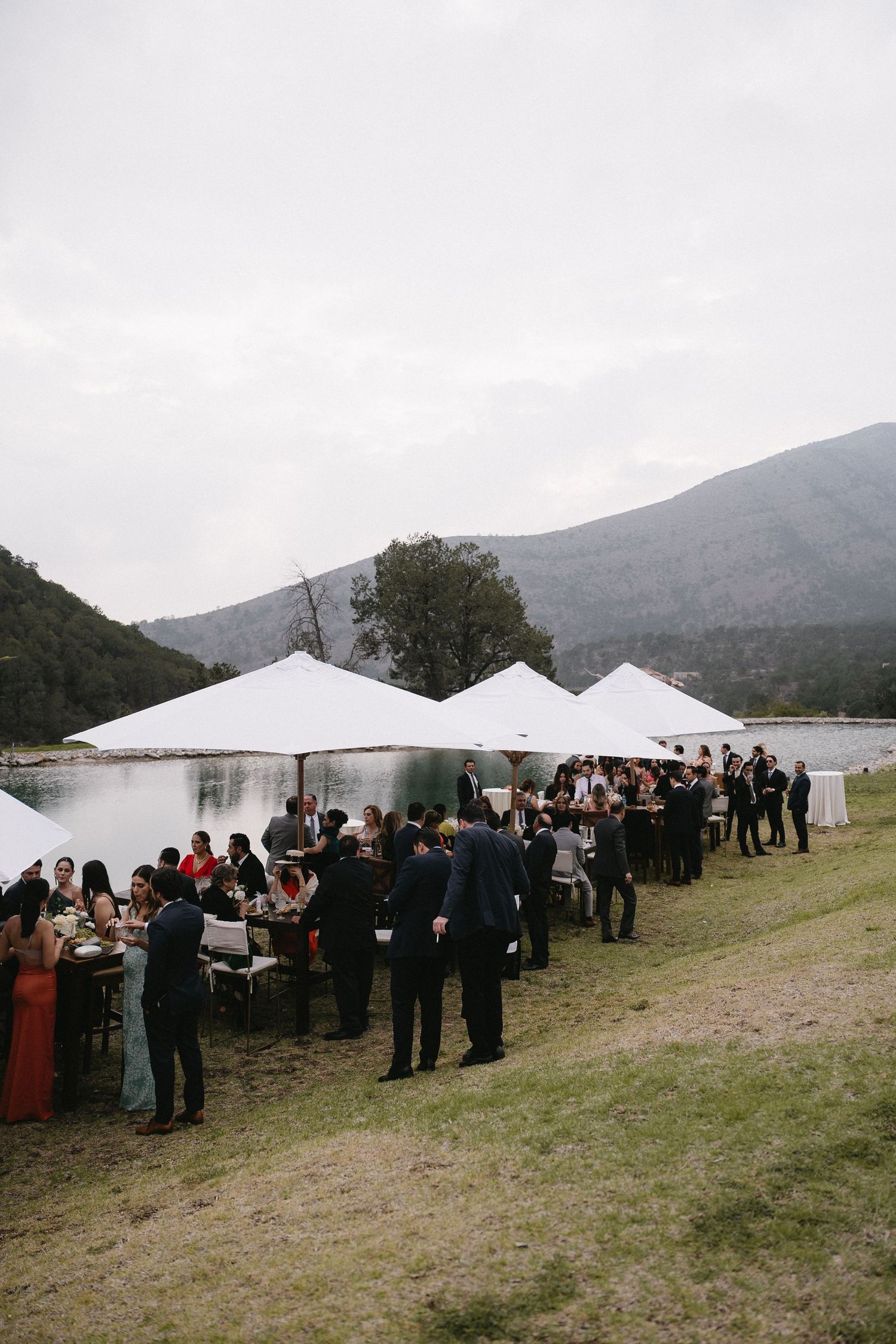 Outdoor wedding reception with white tents set up near mountains and a lake.