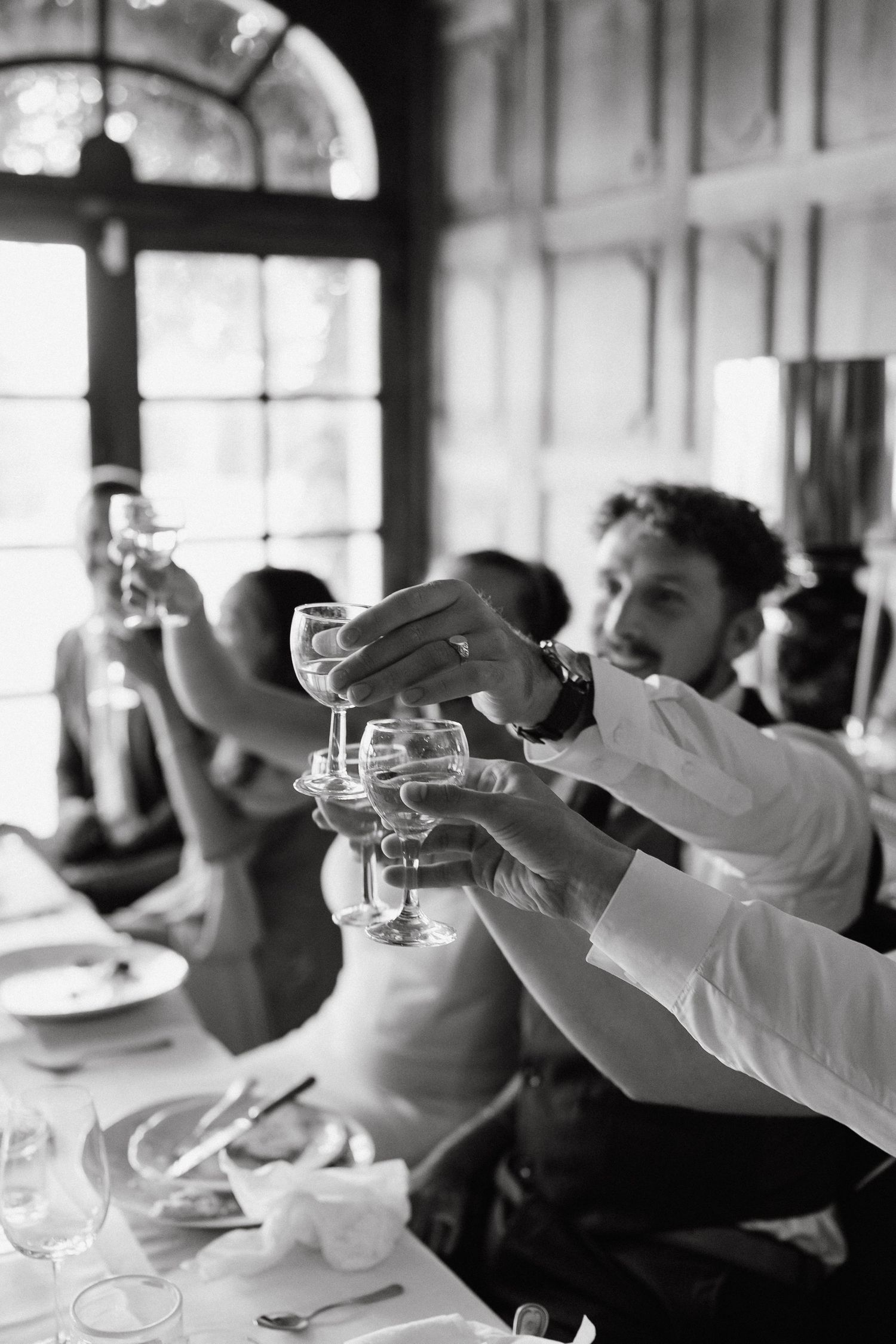 Wedding guests raising champagne glasses for a toast in black and white.