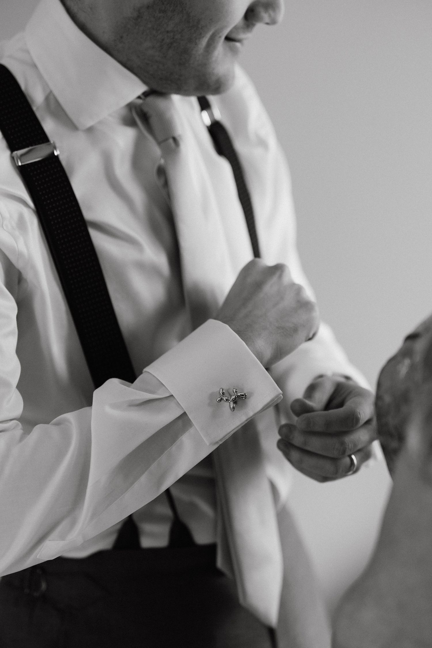 Detail shot of a groom adjusting his tie and cufflinks while getting dressed.