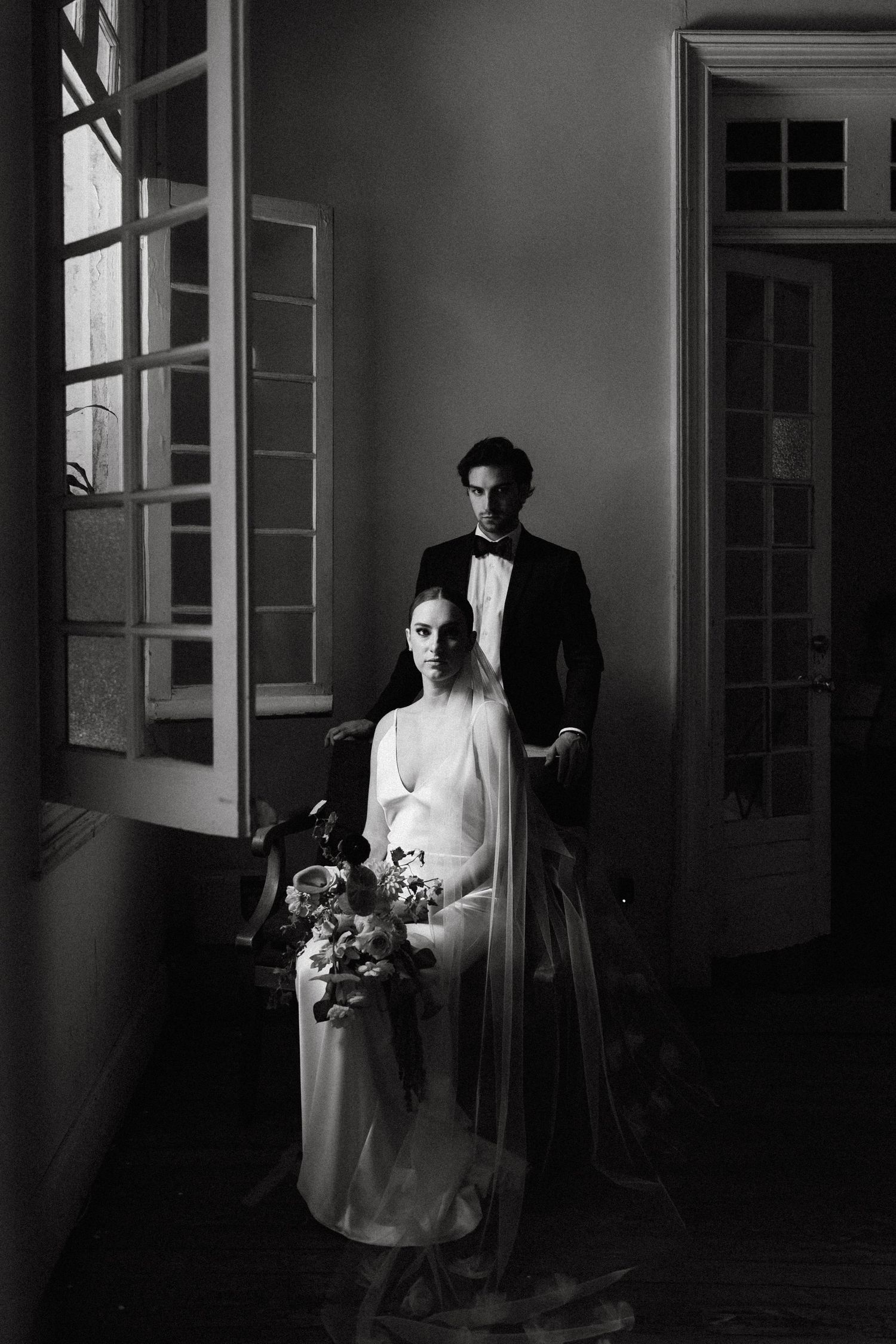 Dramatic black and white wedding portraits in a shadowy corridor with natural window light.