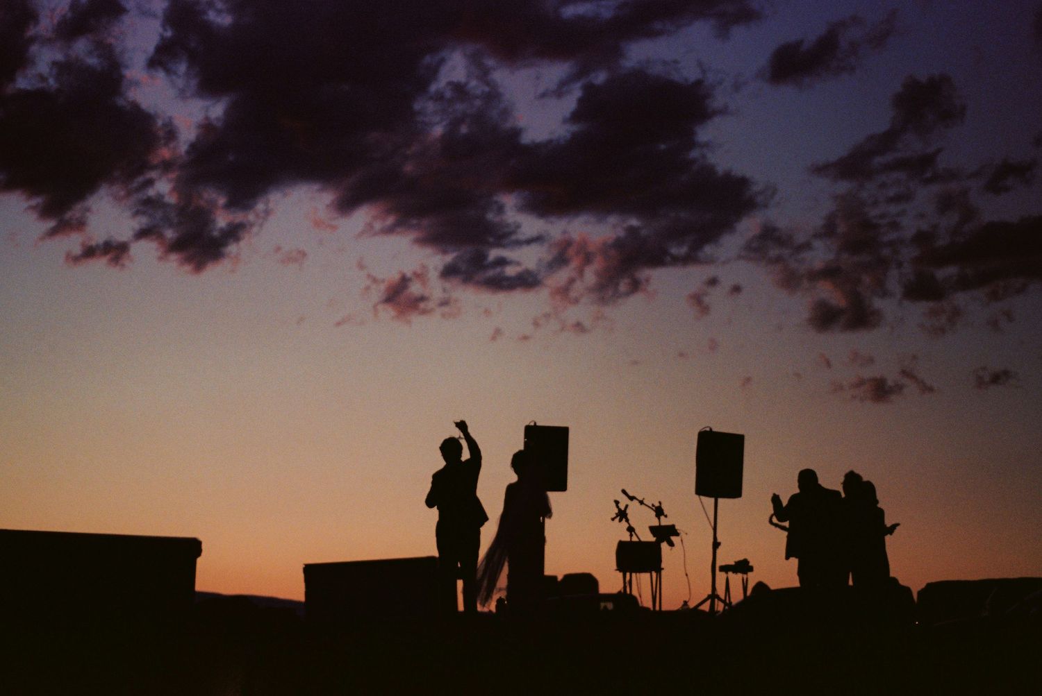 Silhouettes of people against a dramatic sunset sky with dark clouds and vibrant orange hues.