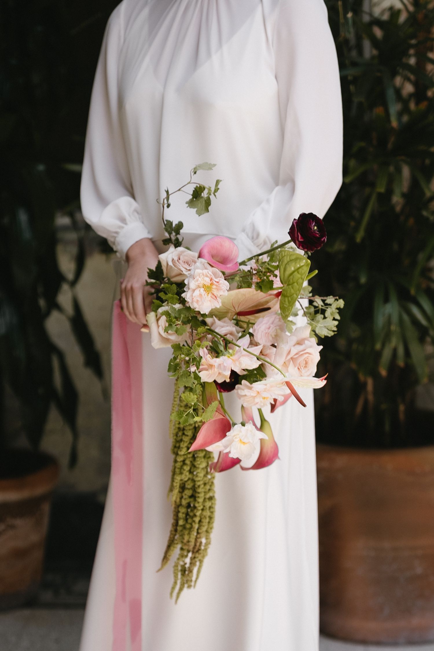 Person in white dress holding romantic bouquet with pink flowers and trailing greenery.