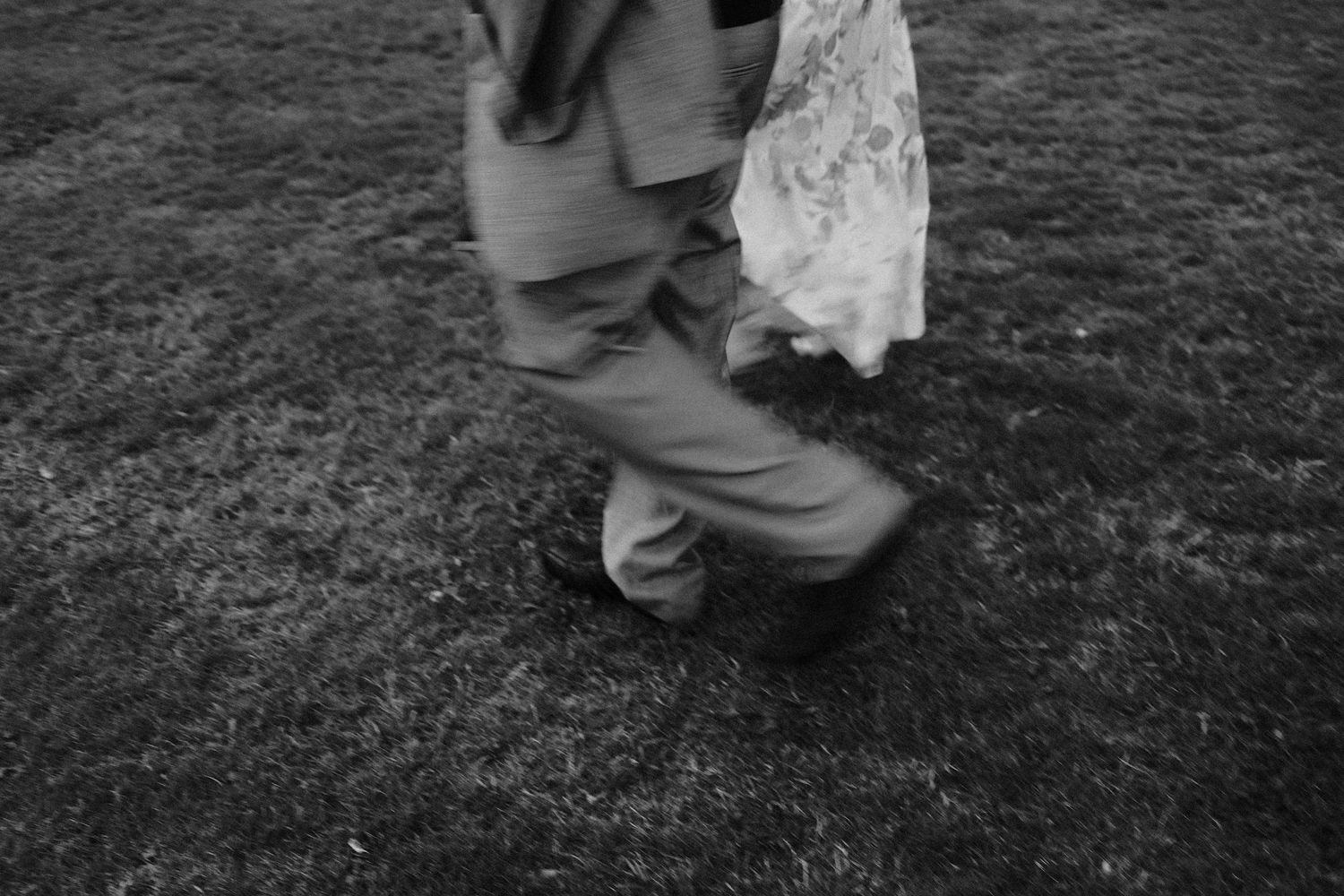 Close-up black and white shot of dancing feet on grass at a wedding.