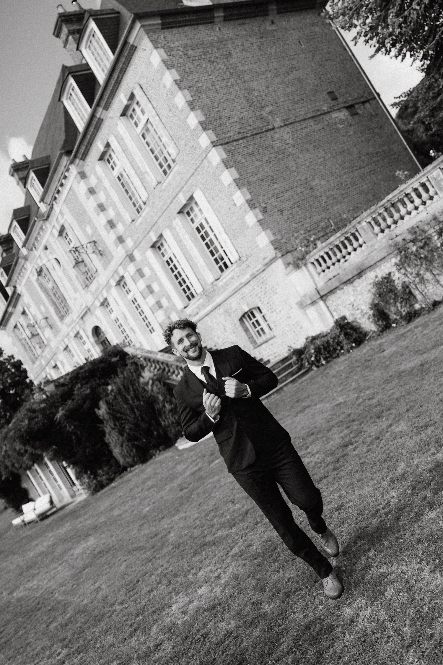 A black and white photo of someone jumping joyfully outside a historic mansion.