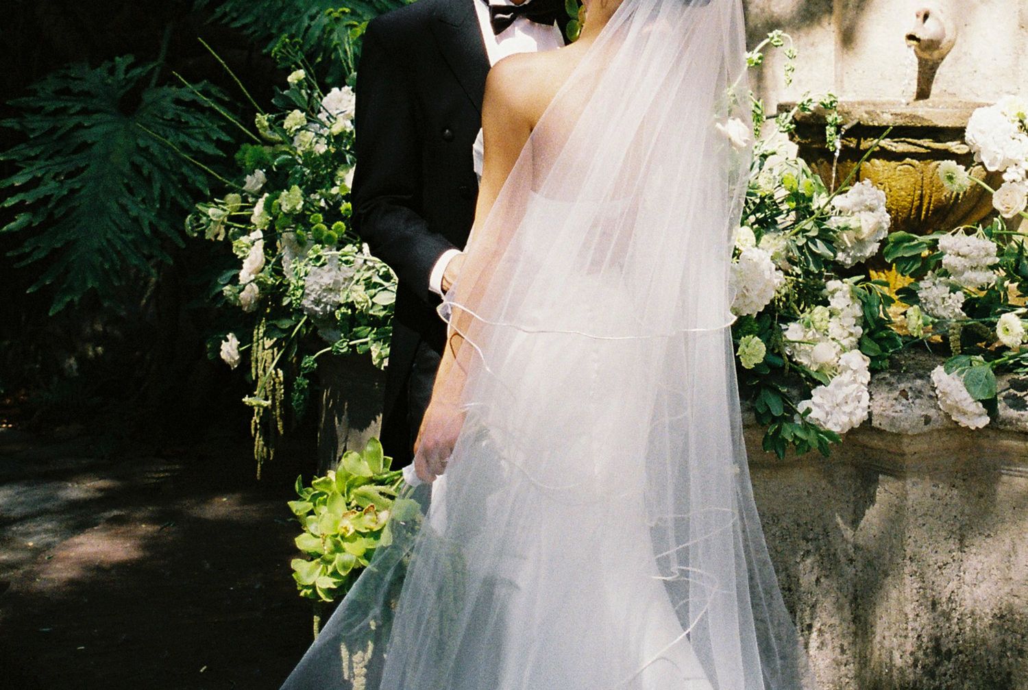 Wedding dress details with flowing veil and floral decorations in garden setting.