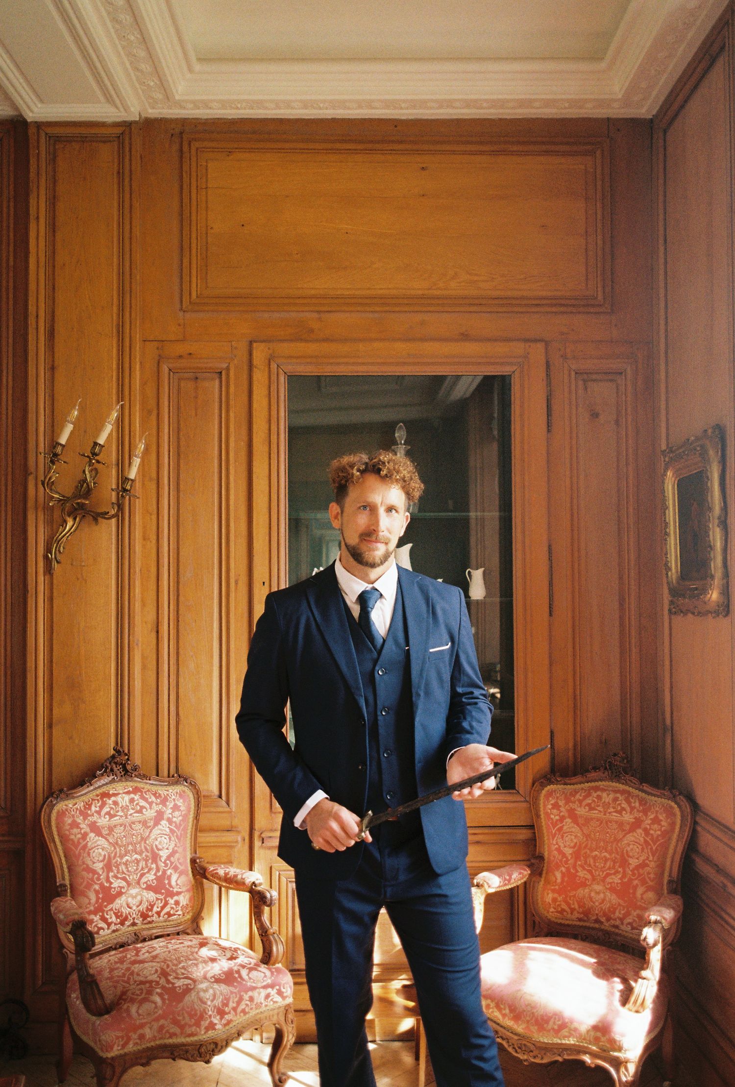 A sequence of five photos showing a person in a blue suit posing against ornate wood-paneled walls with antique furniture.