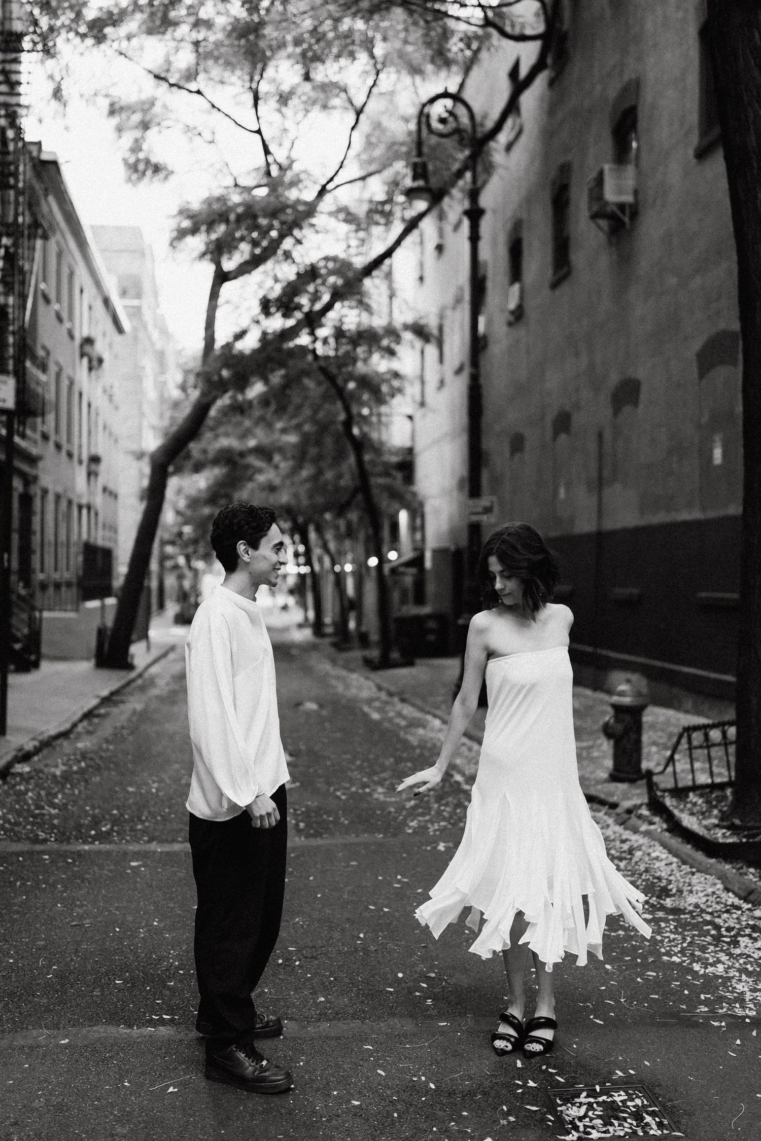 Romantic black and white street scene with couple walking down tree-lined path.