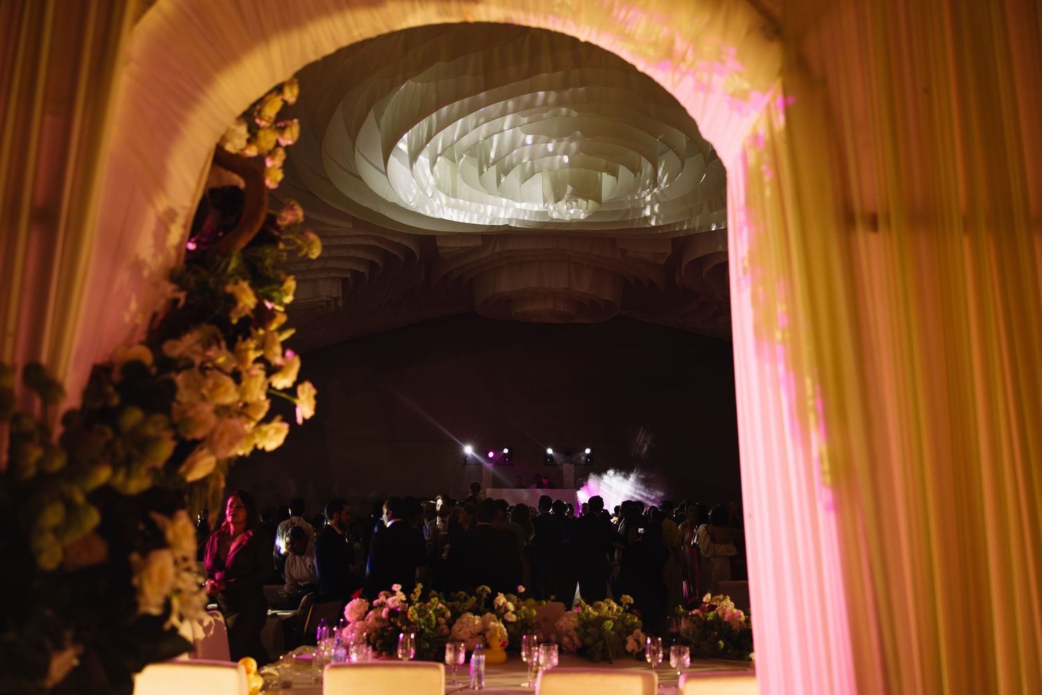 An elegant wedding reception venue with draped fabric and dramatic lighting through an archway.
