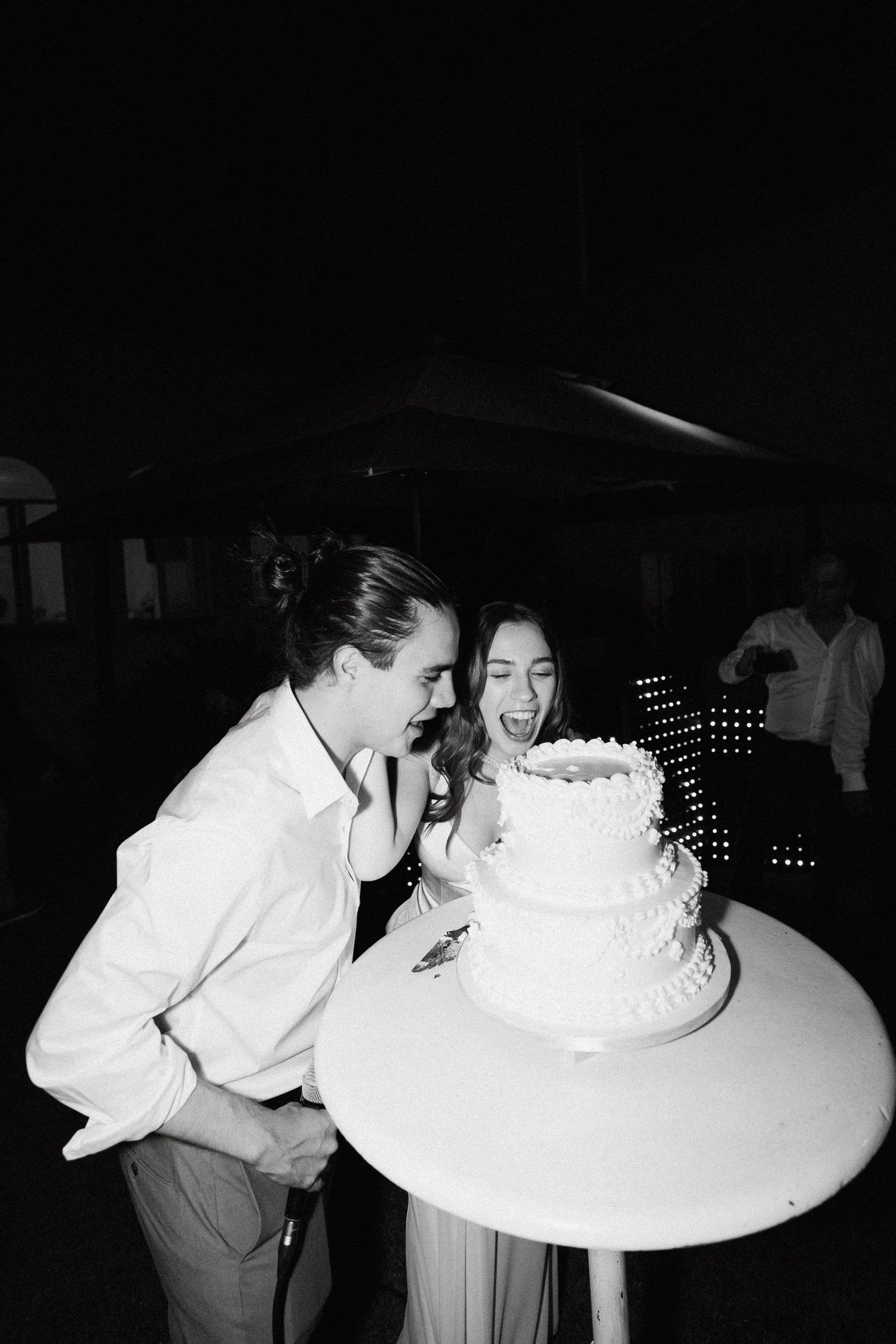 Black and white photo of couple sharing a playful moment with wedding cake.