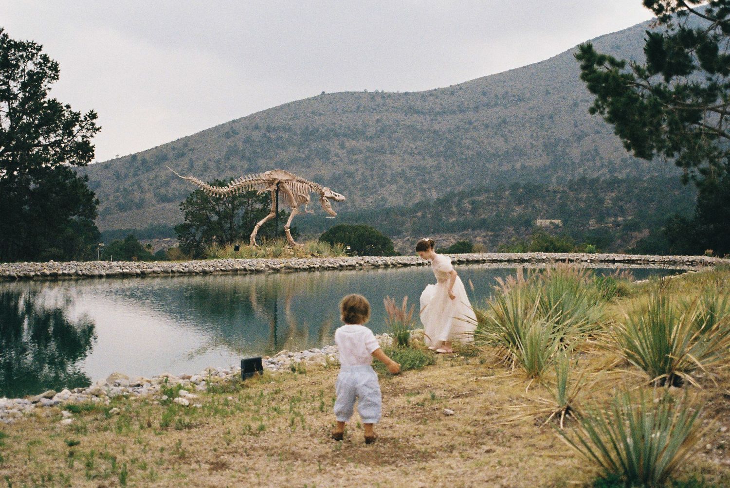 People enjoying a lakeside moment with mountains in the background on a cloudy day.