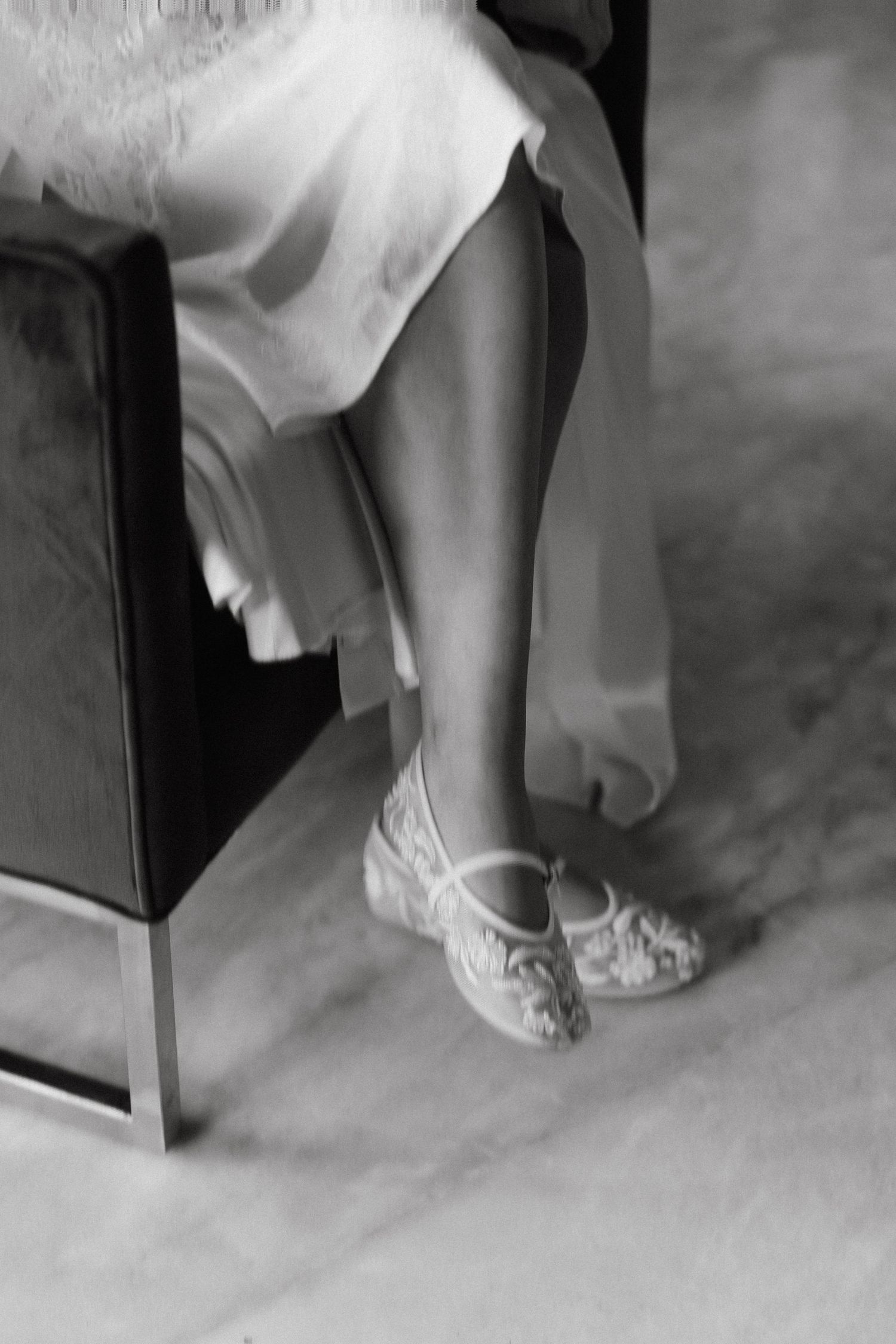 Black and white detail shot of embellished bridal shoes under a flowing dress hem.
