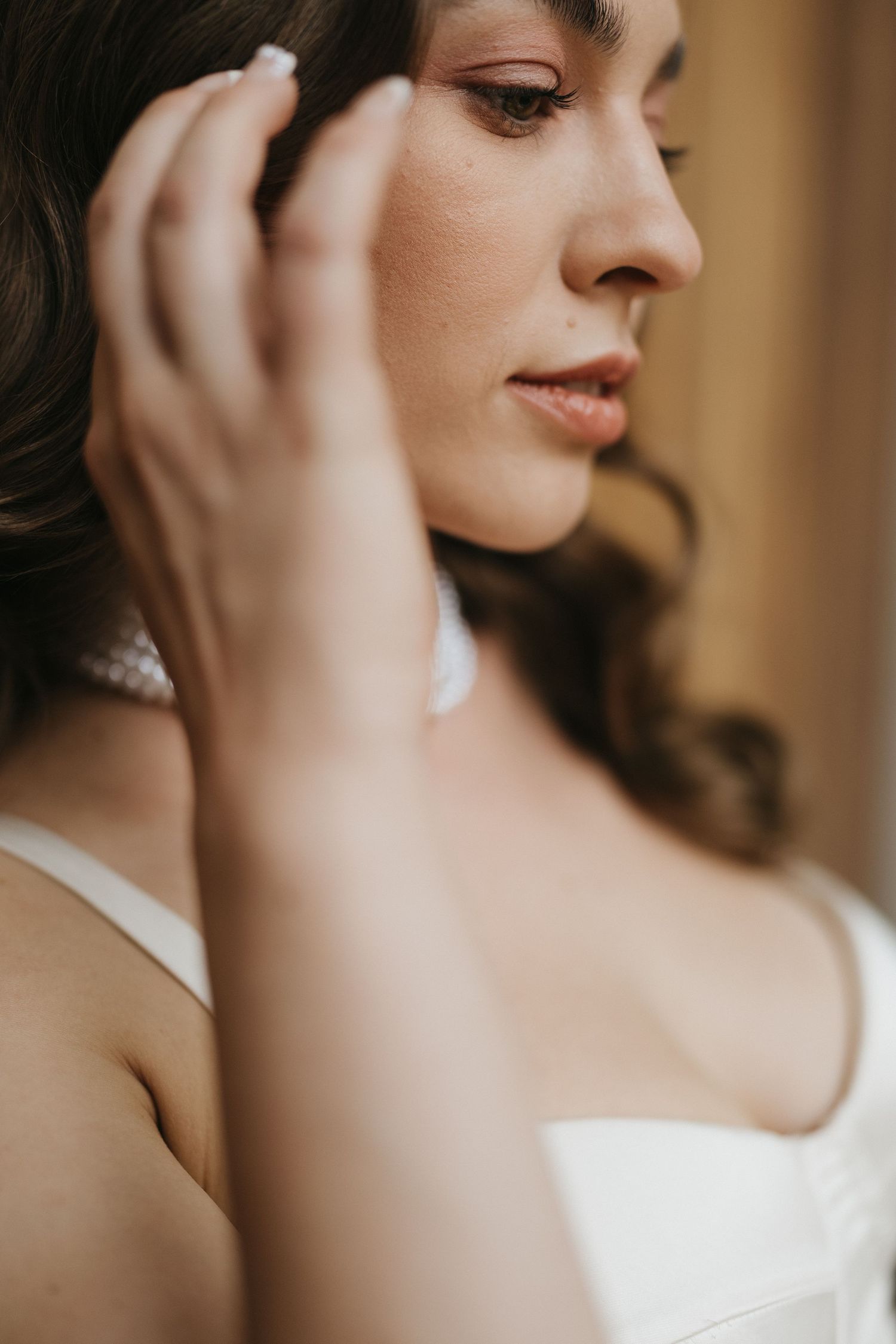 Close-up details of bridal jewelry and makeup in warm tones.