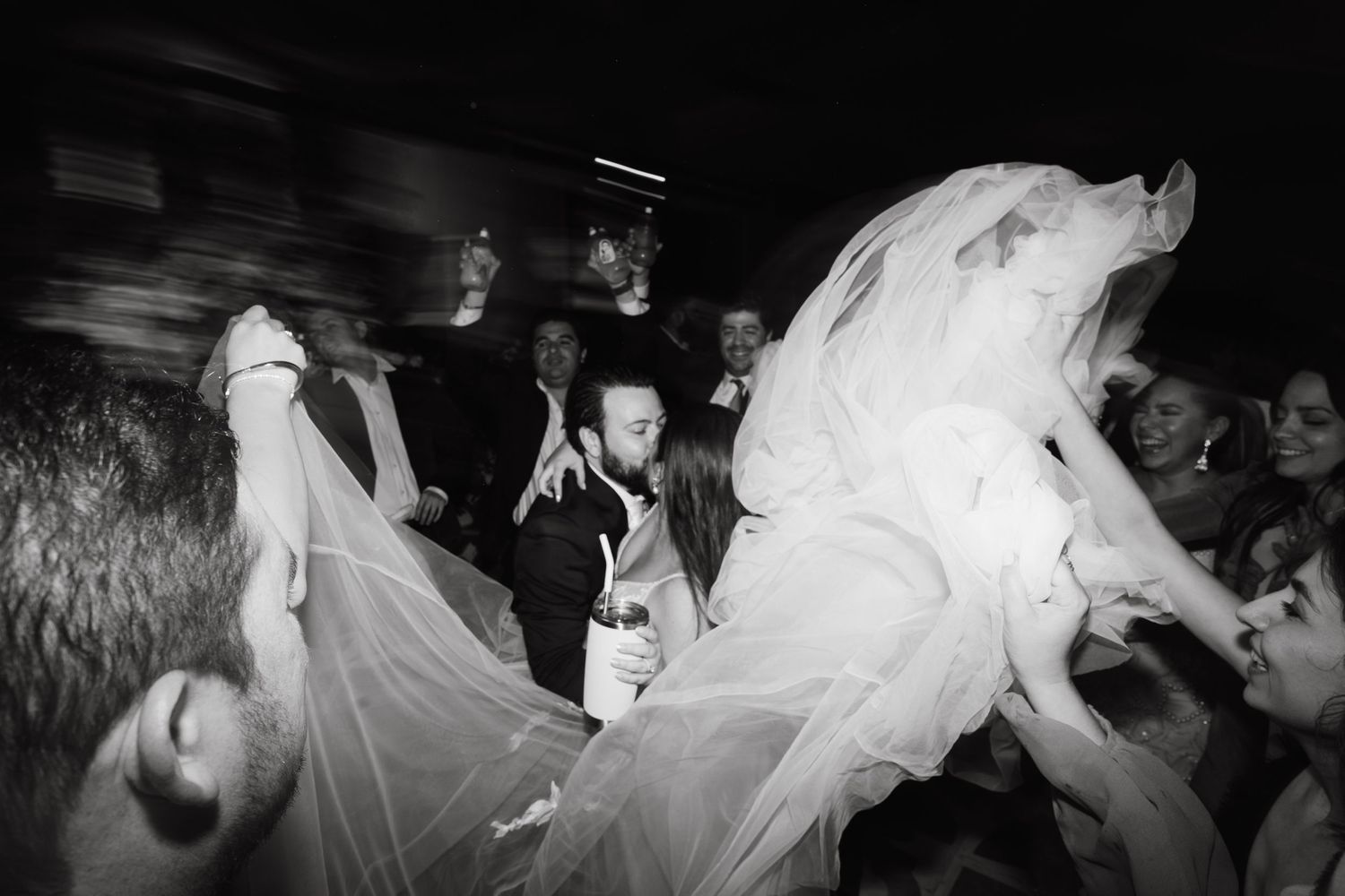 Black and white wedding dance floor scene with guests celebrating under draped fabric decor.