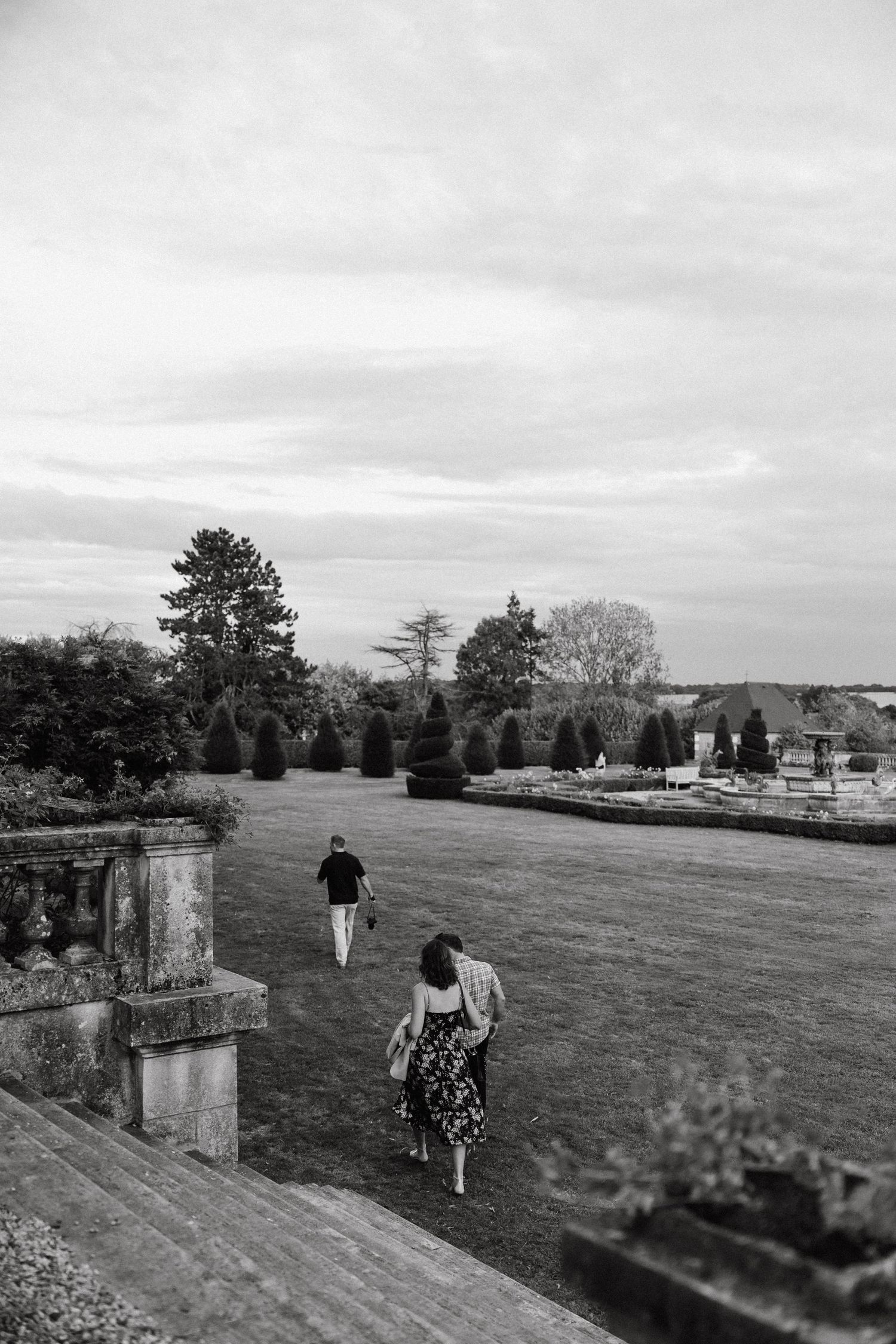 People walking along a grassy path on an overcast day with stone pillars and trees in the distance.