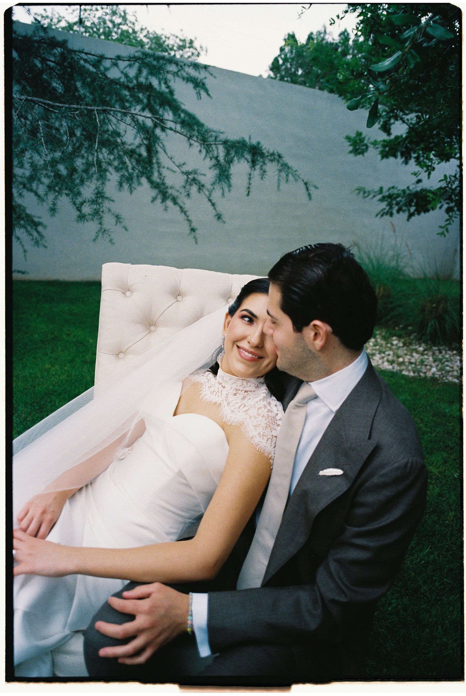 Romantic couple poses on pink tufted couch in outdoor garden setting.