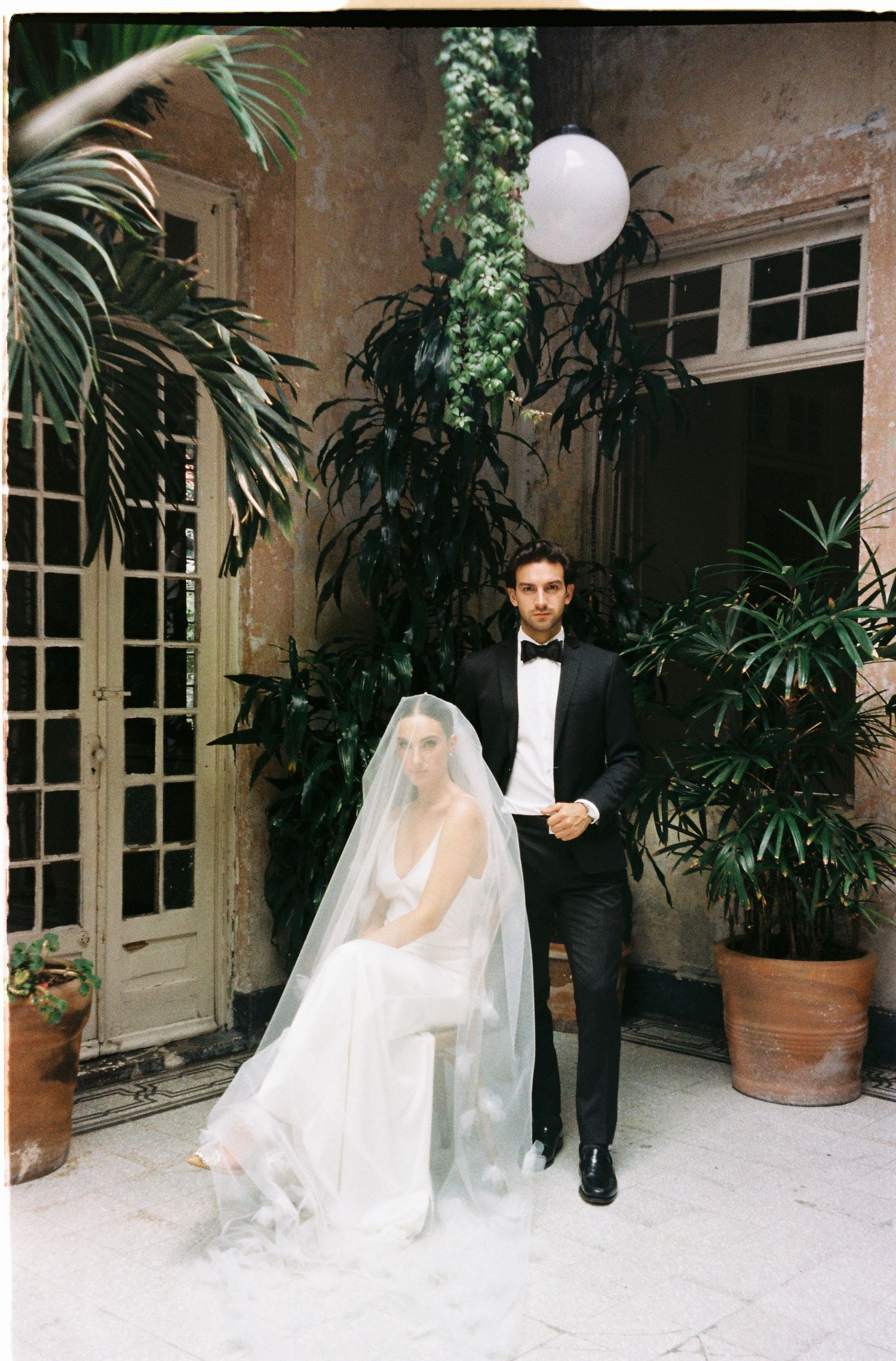 Wedding couple in formal attire photographed in sequence against a stone courtyard with tropical plants.