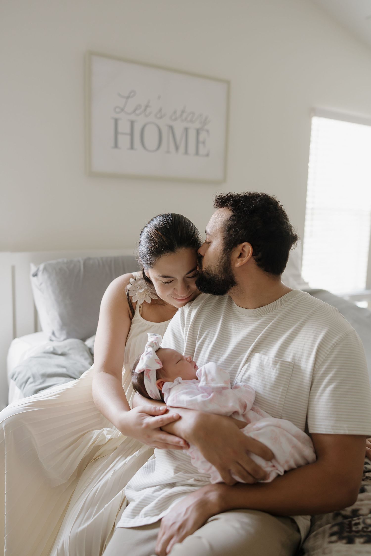 A tender family moment captured in soft light as parents cuddle with their newborn baby on a cozy bed.
