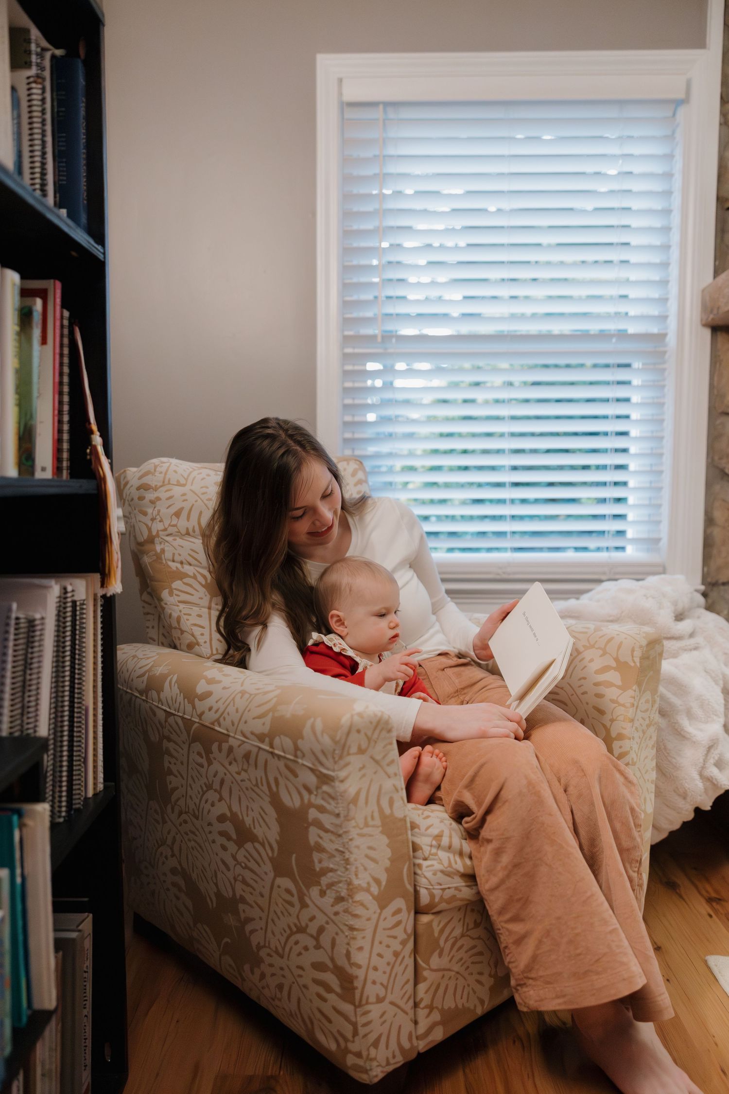 Parent and child share a tender moment reading together on a patterned couch near a window.