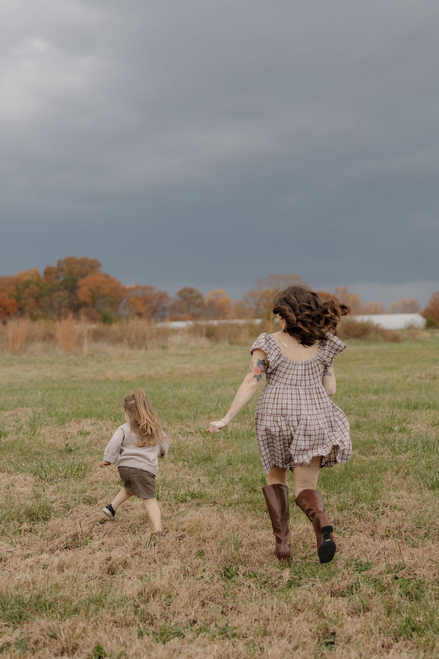Two people run playfully through a golden autumn field under moody gray skies.