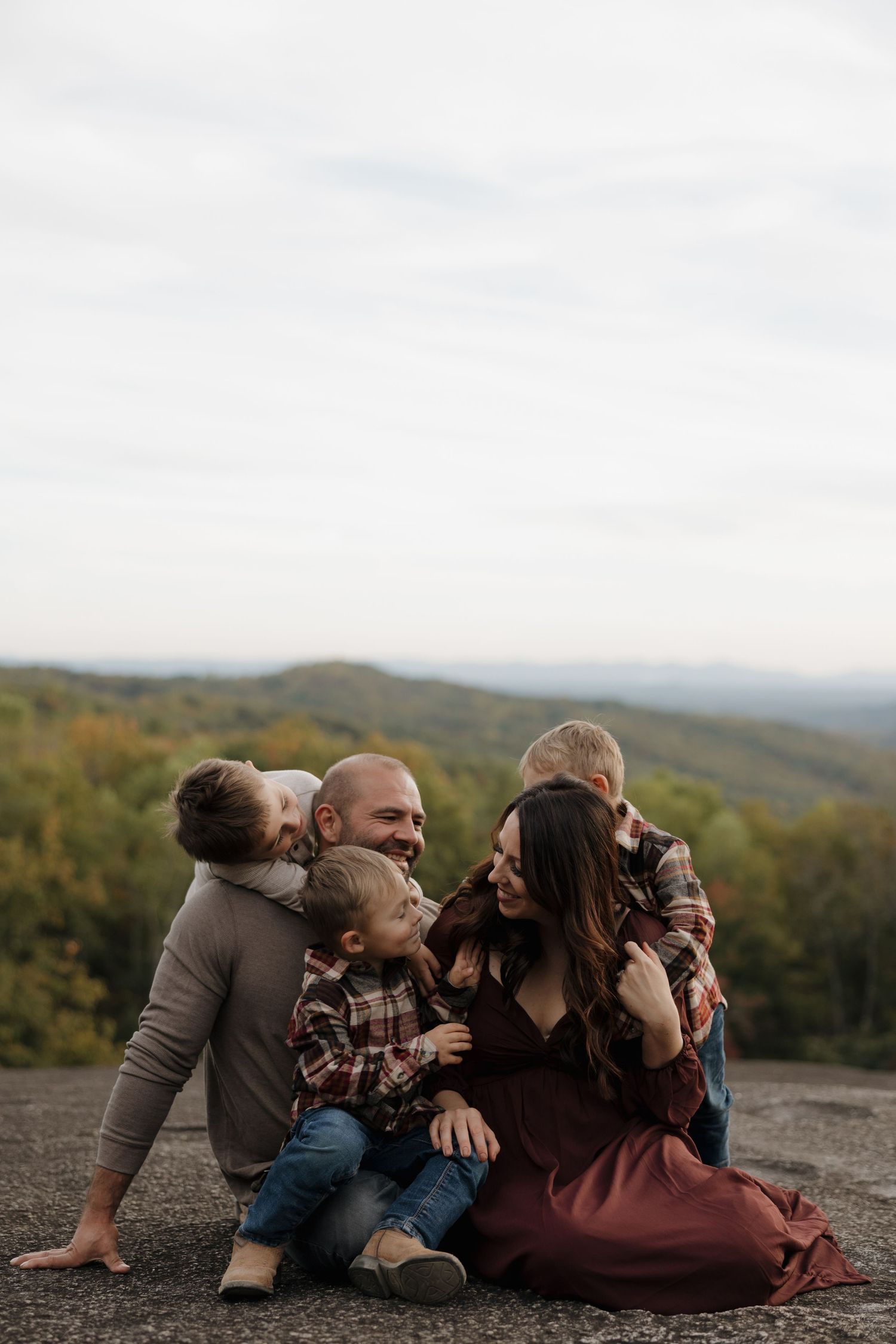 Family enjoying a tender moment together while sitting on rocks overlooking scenic mountain views during autumn.