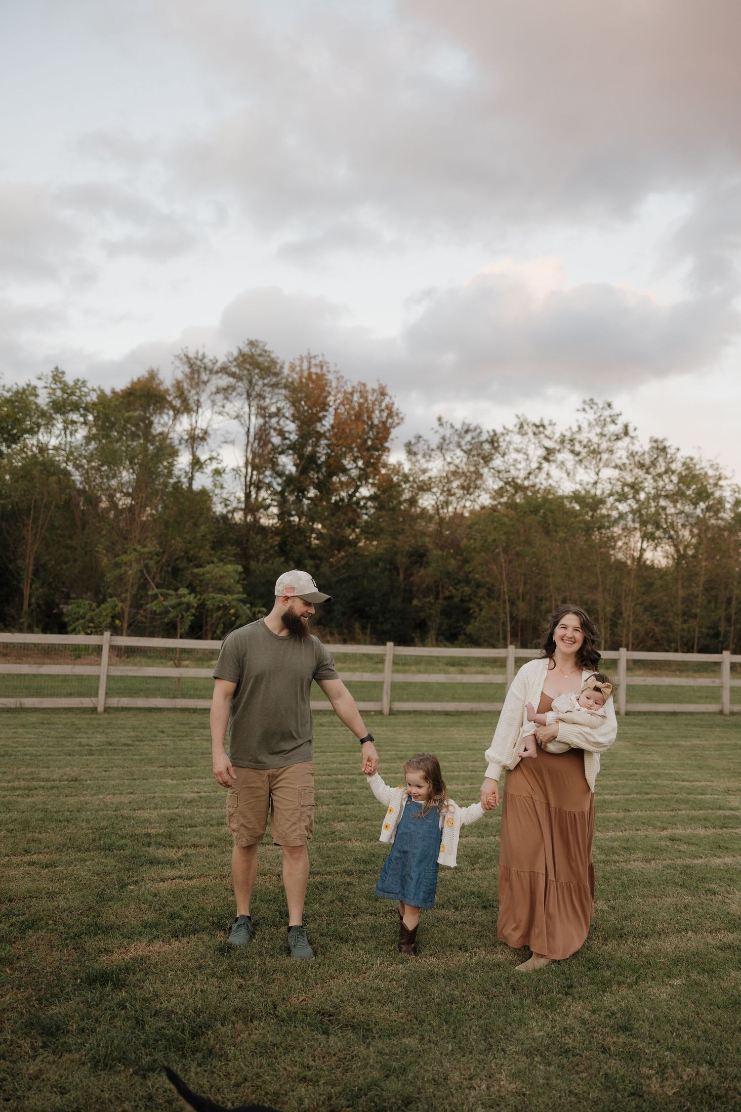 Family walking together in an open grassy field at sunset with autumn trees in the background.