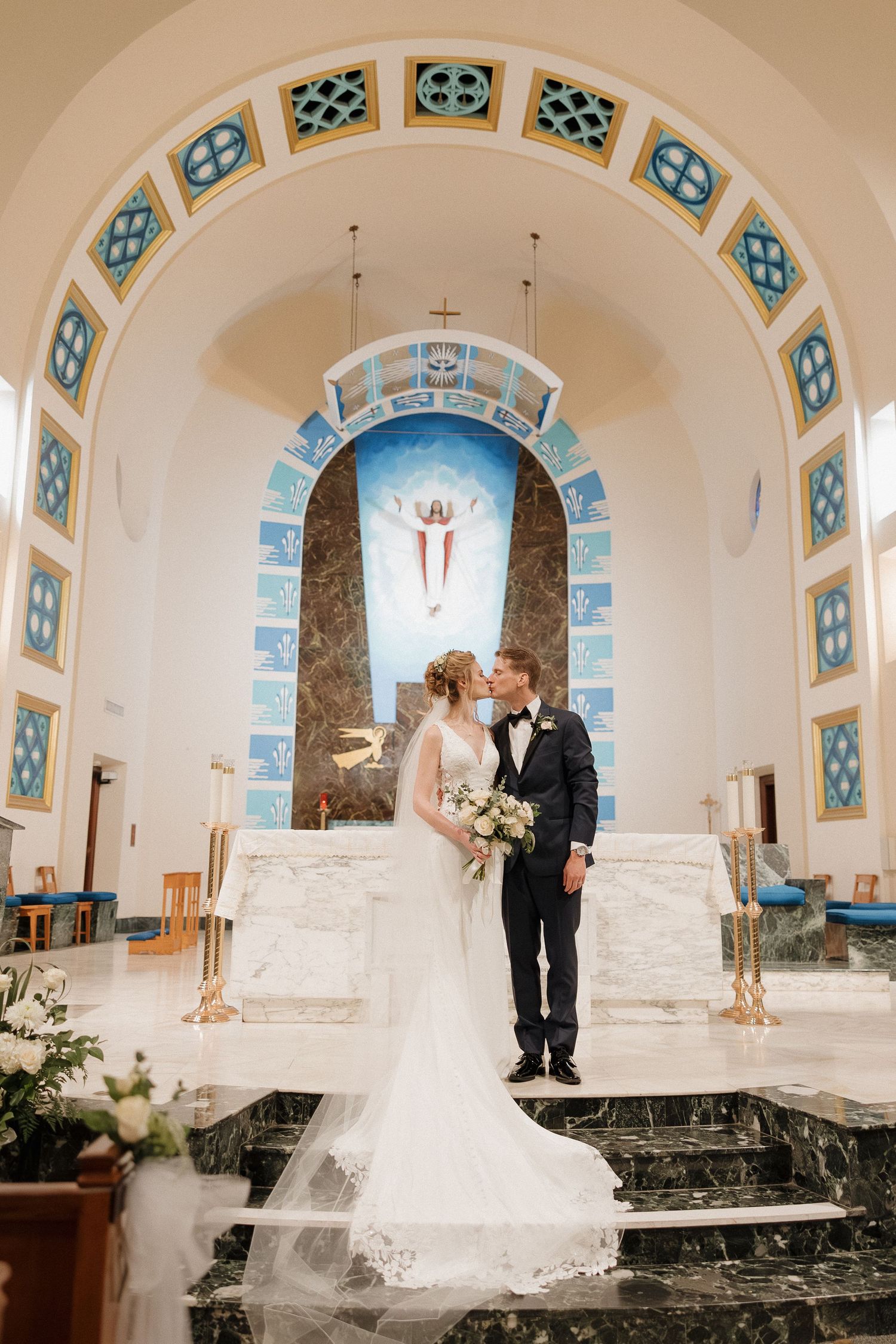 A wedding ceremony in a church with blue stained glass windows and arched architecture.