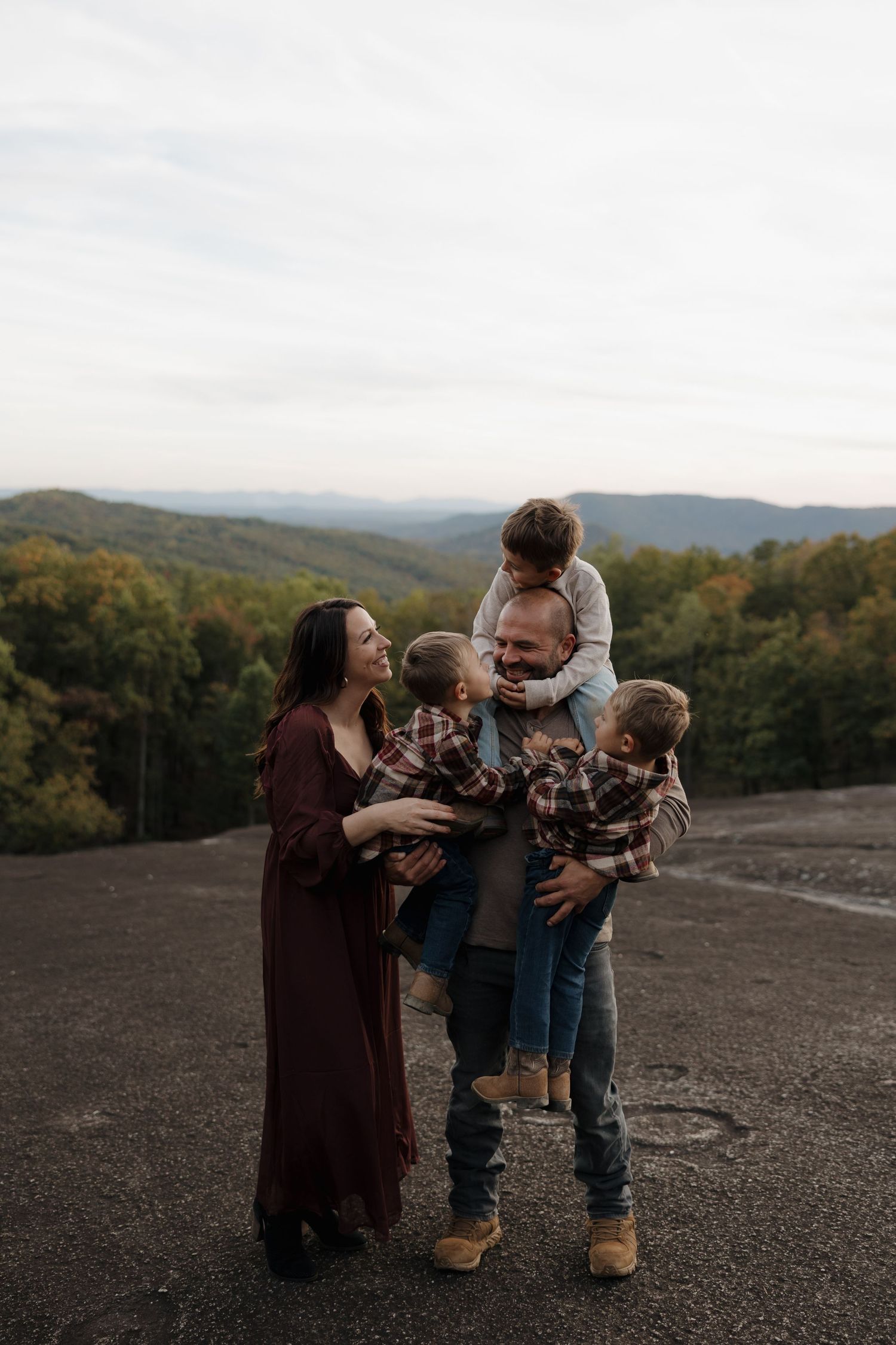 A family shares a tender moment together against a backdrop of rolling mountains and autumn trees at sunset.