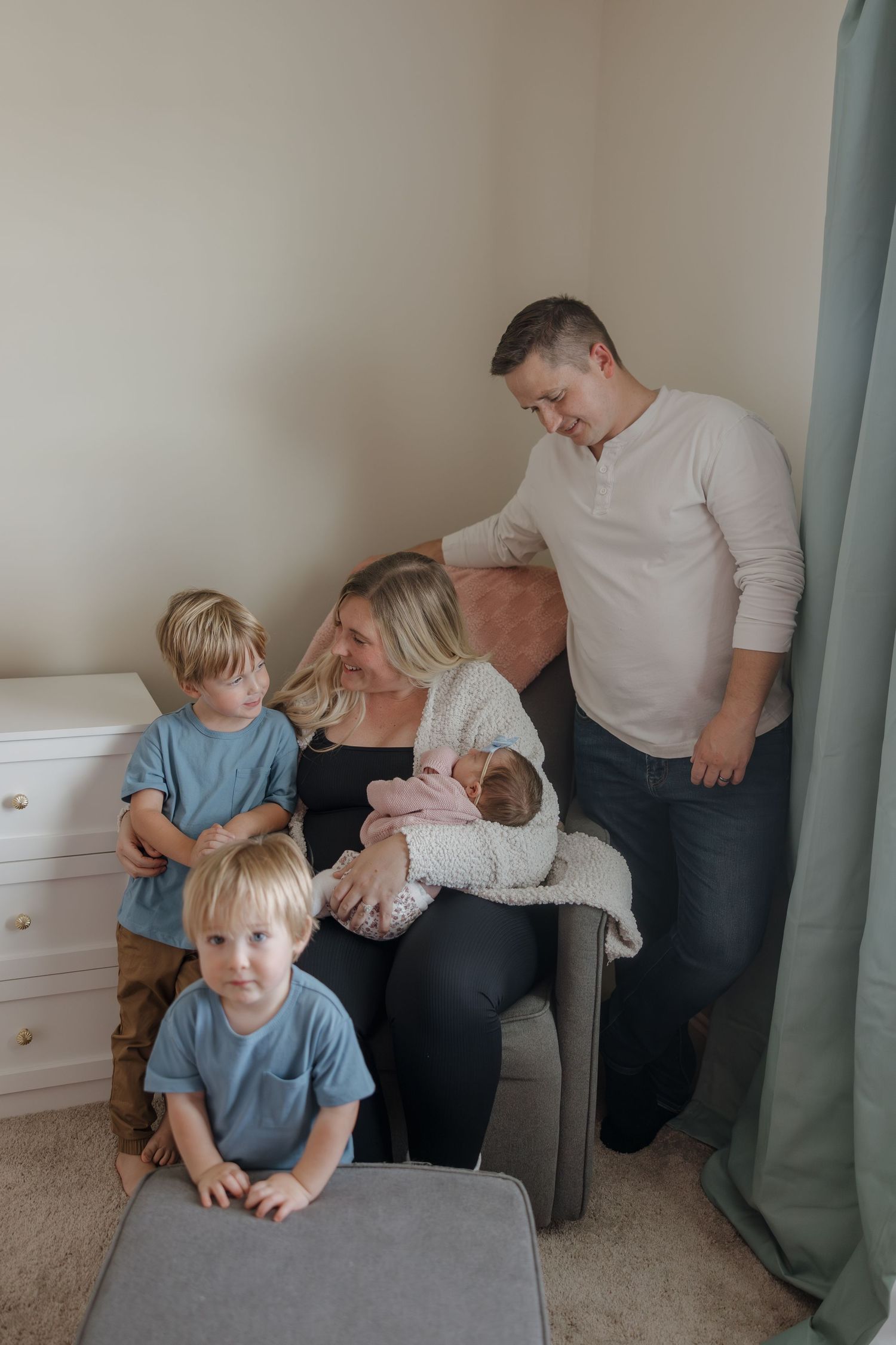A family gathers together in a cozy corner of their home, sharing a tender moment with their newborn baby.