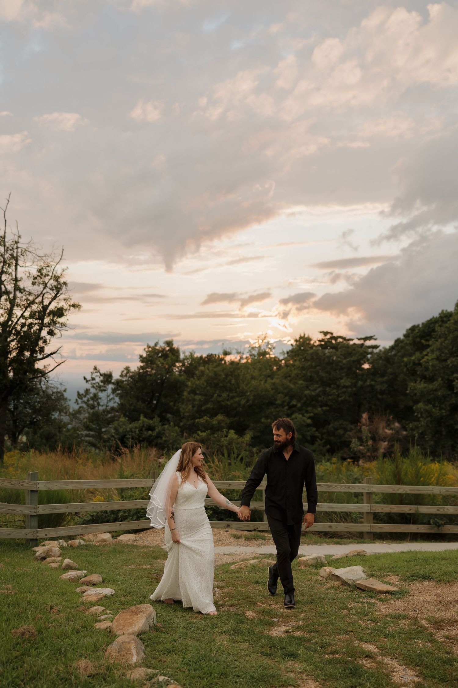 A couple walks along a stone path during golden hour with a beautiful sunset sky behind them.