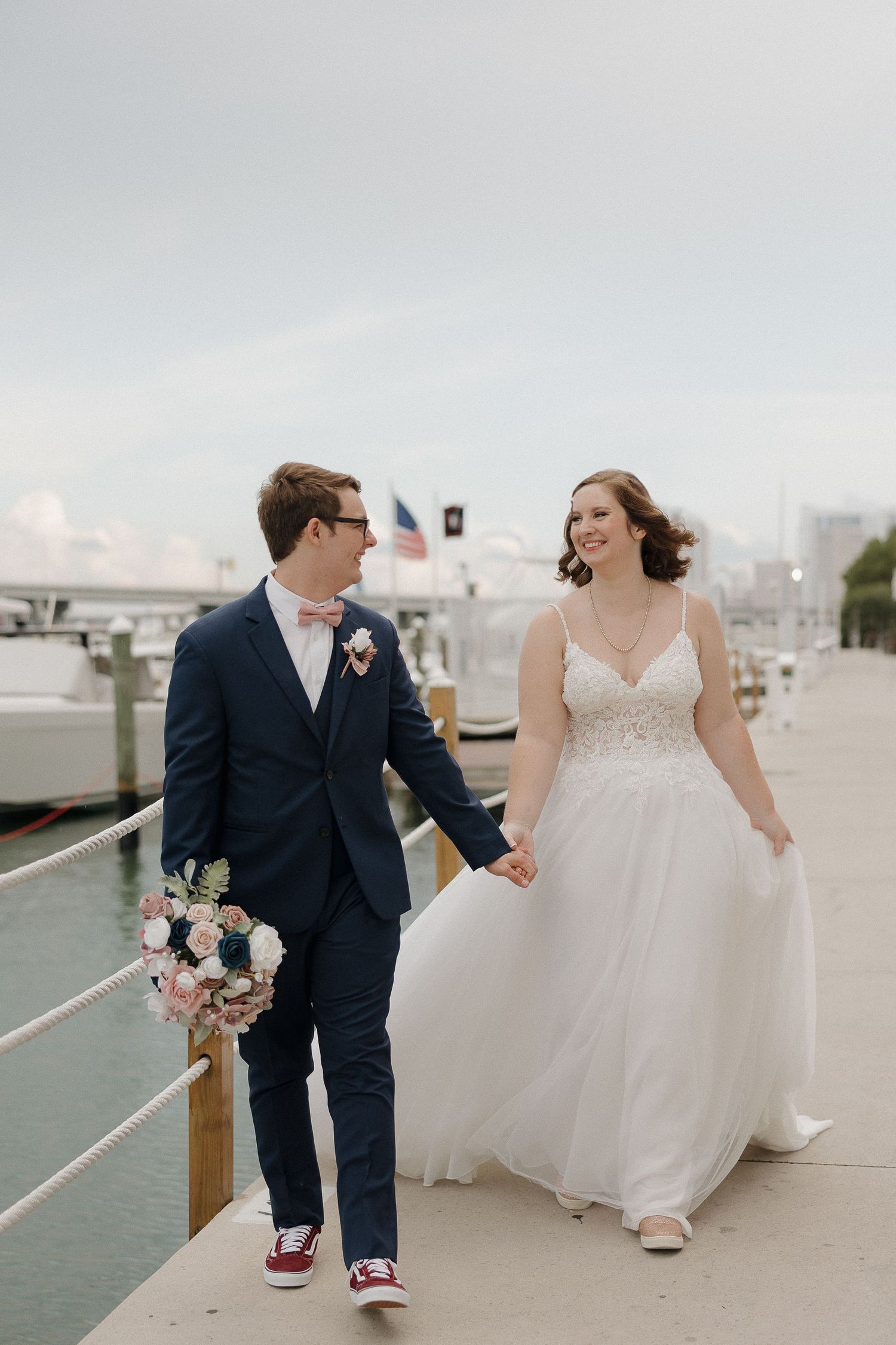 Newlyweds walking along boardwalk with bride in white dress and groom in navy suit.