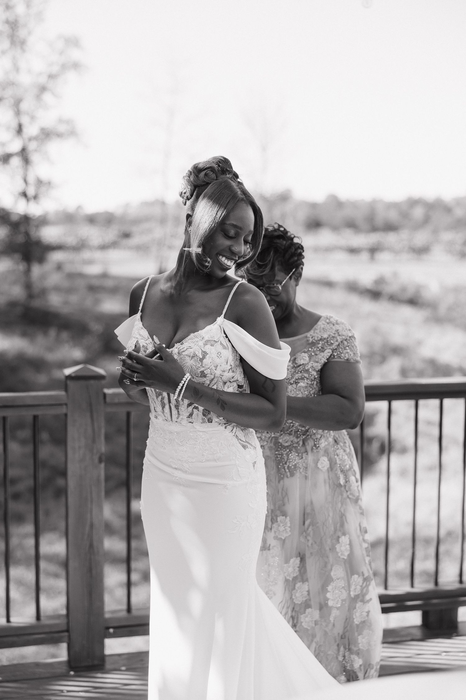 Two people in white dresses share intimate moment on outdoor deck.