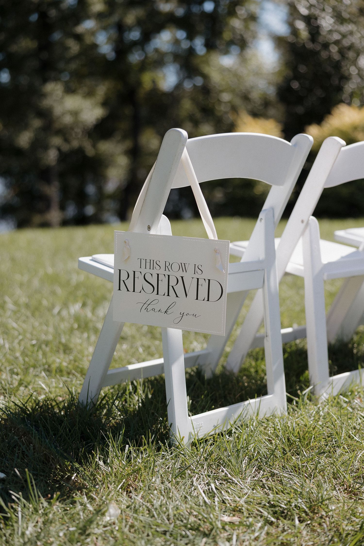 White folding chair with 'Reserved' sign on grassy lawn at outdoor wedding ceremony.
