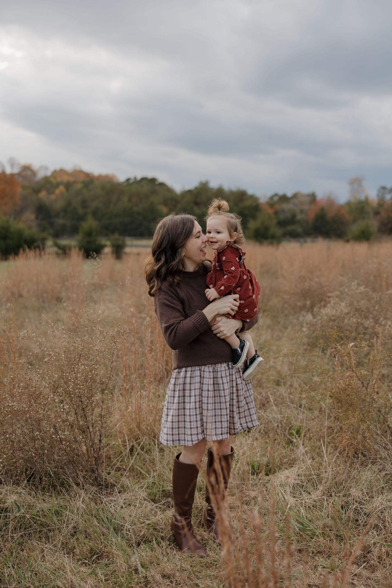 Two people share a tender moment in a rustic autumn field with tall grass and fall foliage in the background.