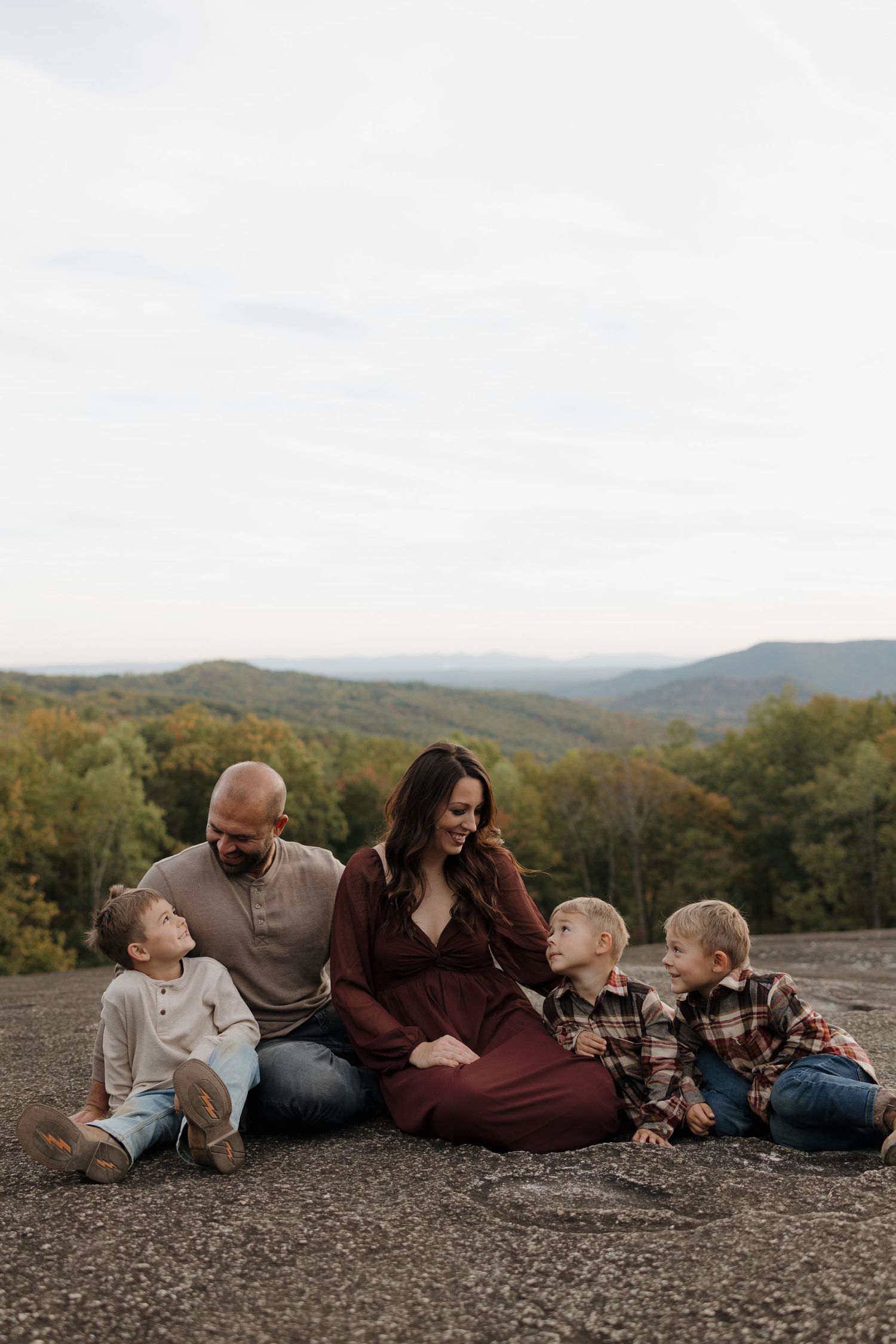 A family sits together on a rocky overlook with autumn mountains and forest in the background.