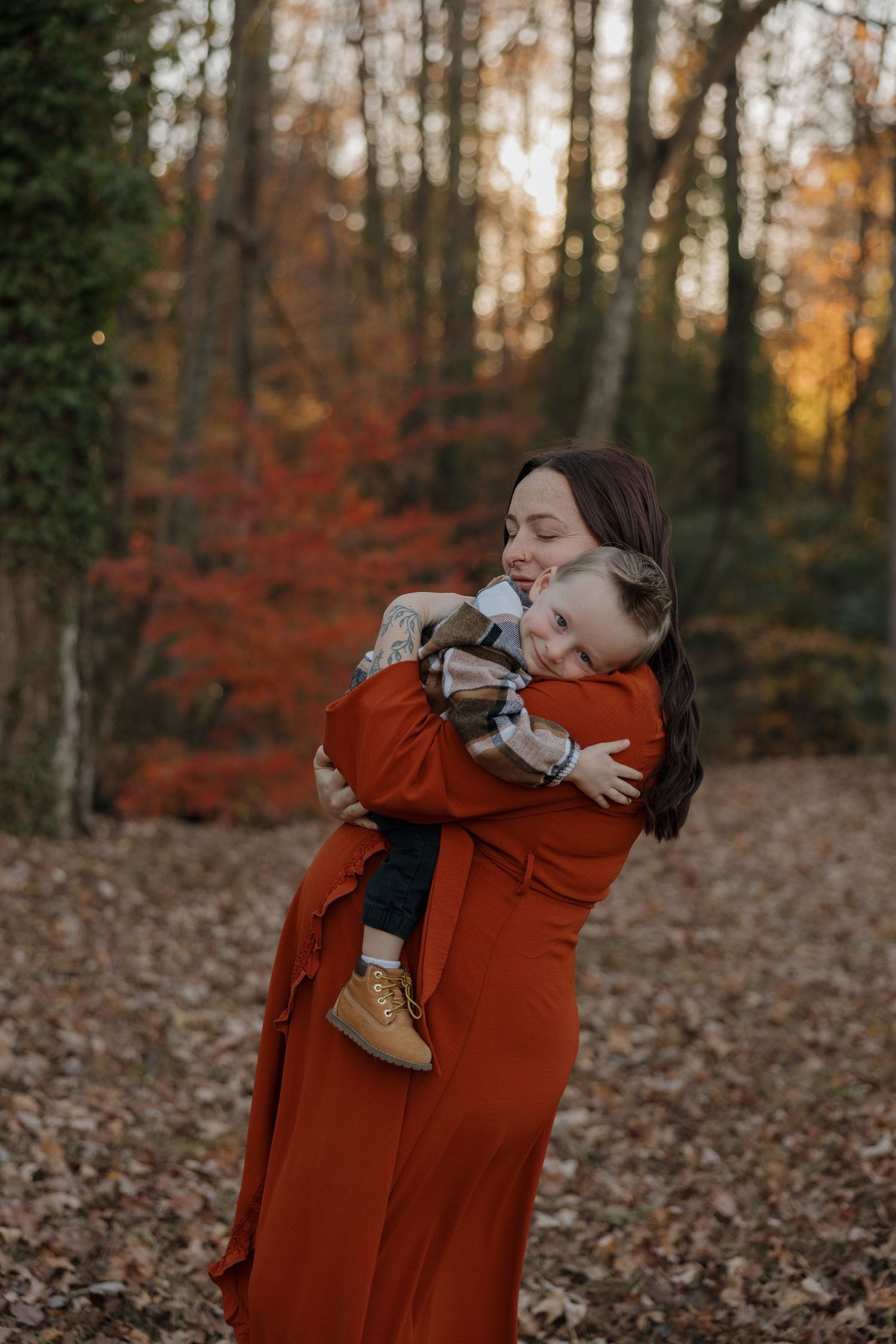 A tender embrace between two figures in a rustic autumn forest setting with red foliage and fallen leaves.