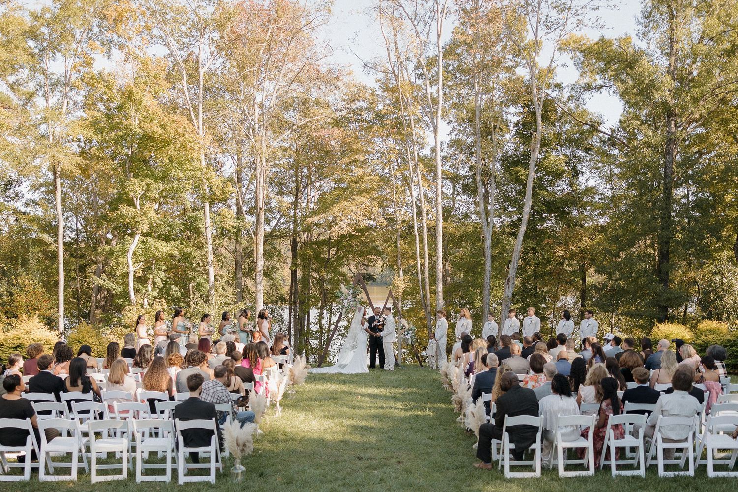 Outdoor wedding ceremony setup with white chairs and fall foliage backdrop.