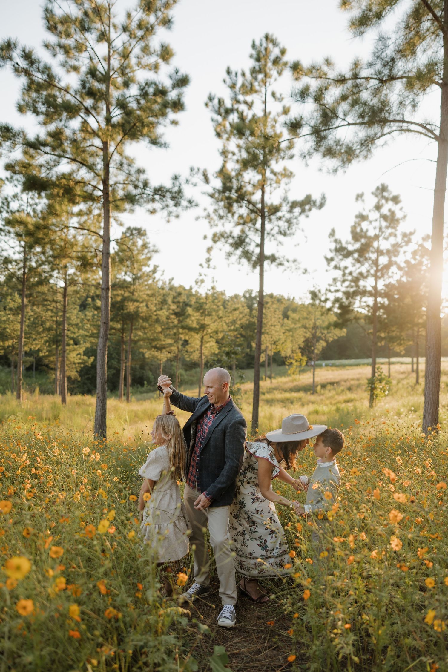 Family of four enjoying a golden hour stroll through a wildflower meadow surrounded by tall pine trees.