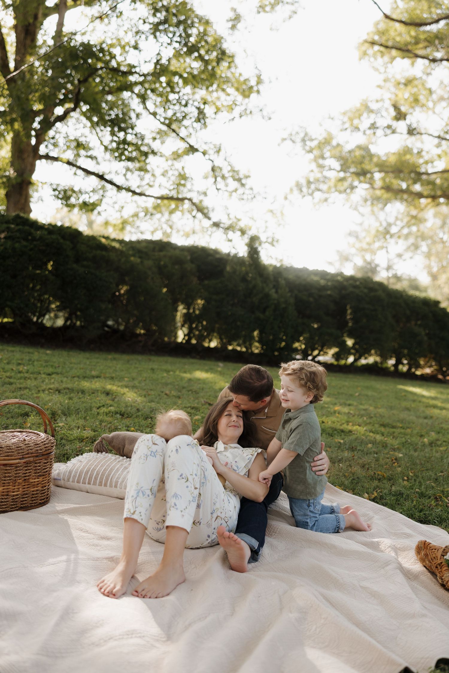 Family enjoying a sunny picnic on a blanket in a lush green park, with parents and child sharing a joyful moment.